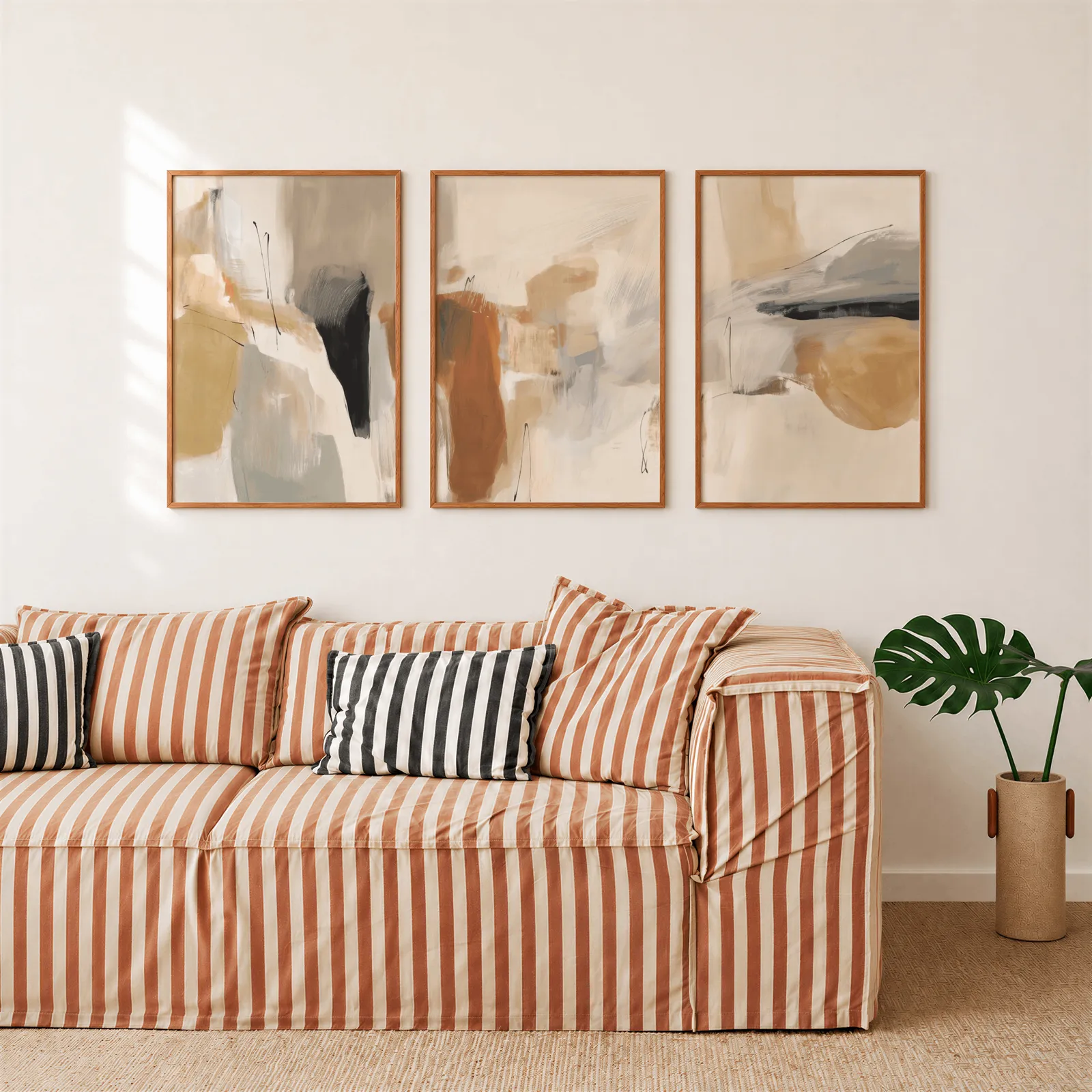 neutral abstract triptych wall art in terracotta and beige, above a rust-striped sofa beside a potted monstera