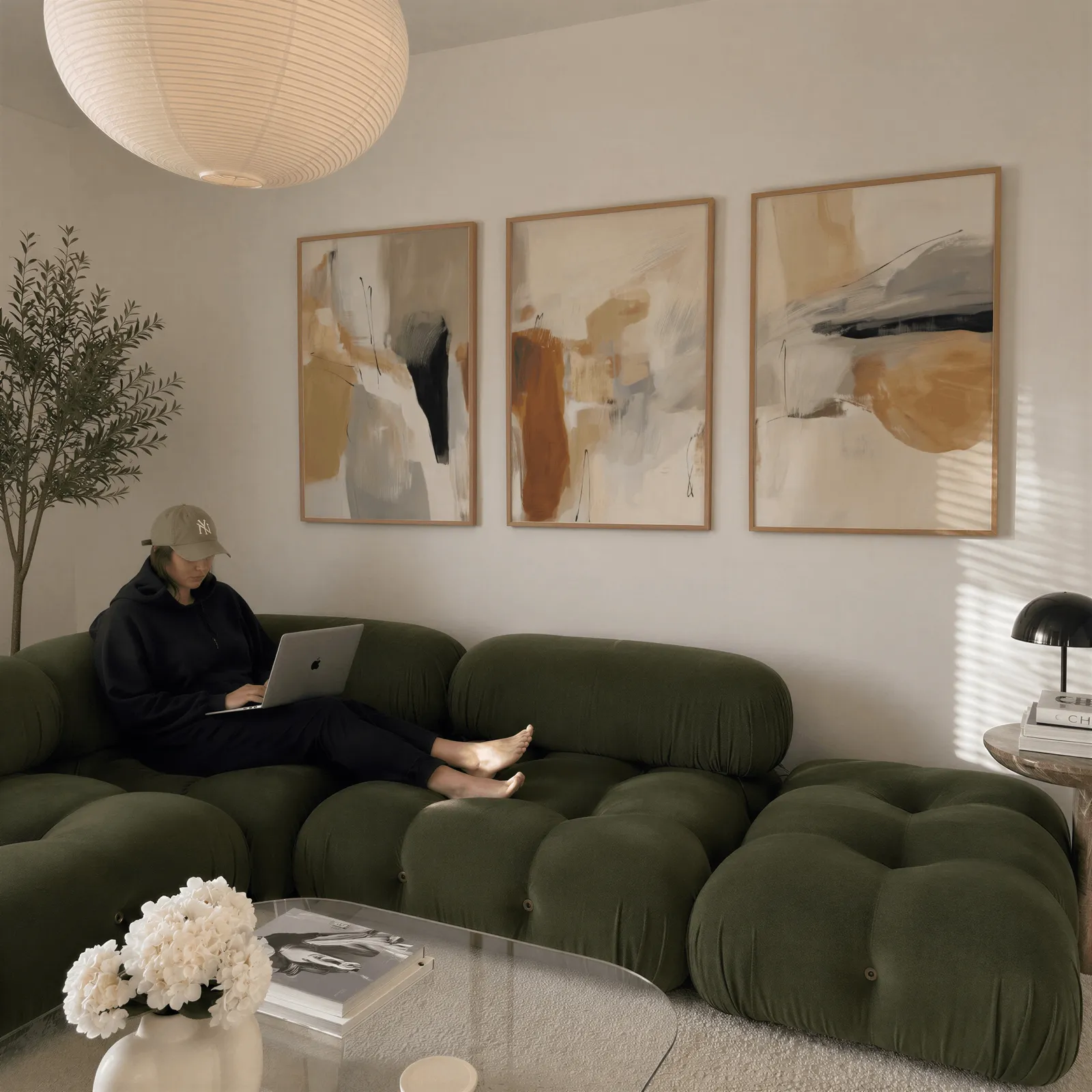 neutral abstract triptych wall art in terracotta and beige, above a plush olive velvet sectional beneath a paper lantern light