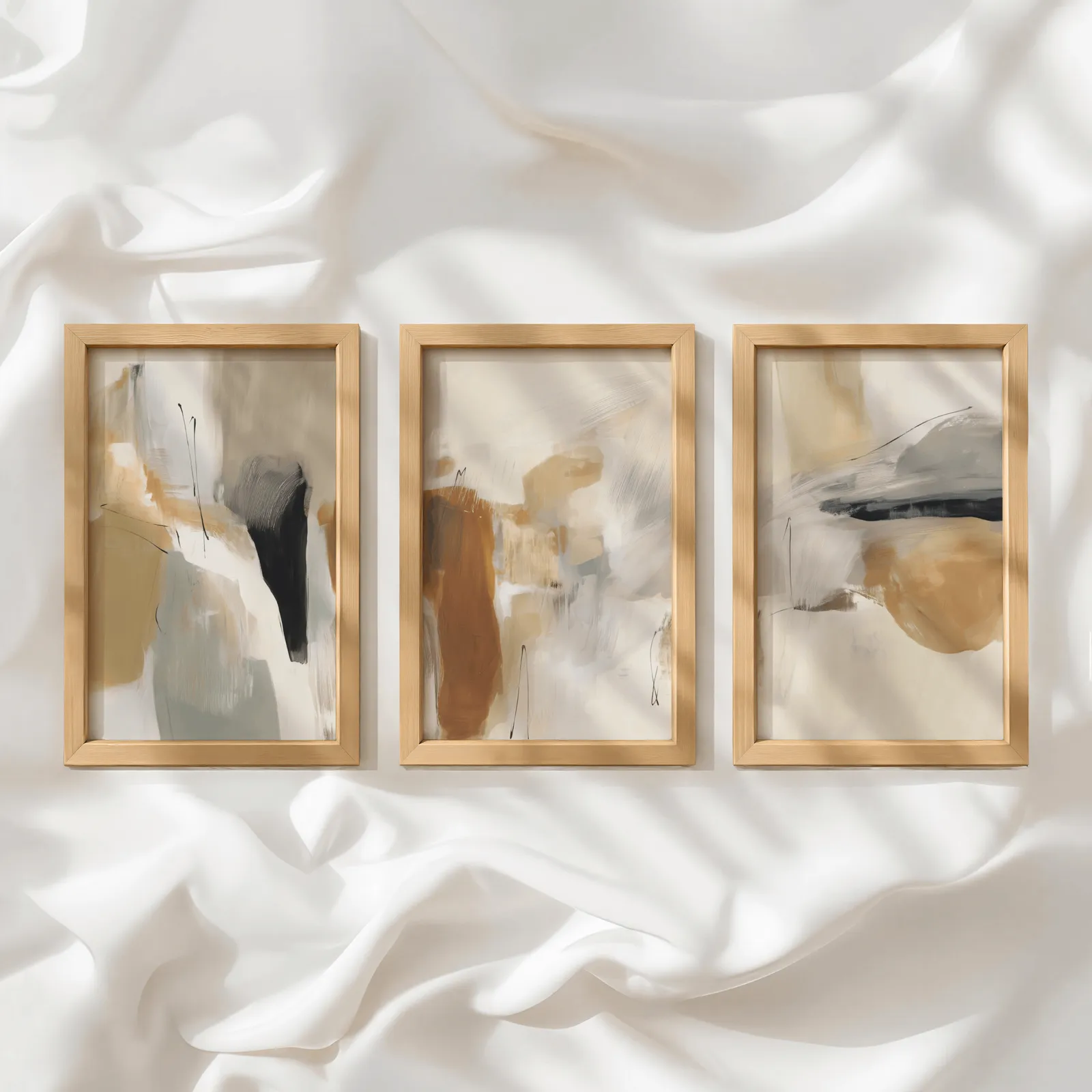 neutral abstract triptych wall art in terracotta and beige, in a row atop rumpled white silky fabric
