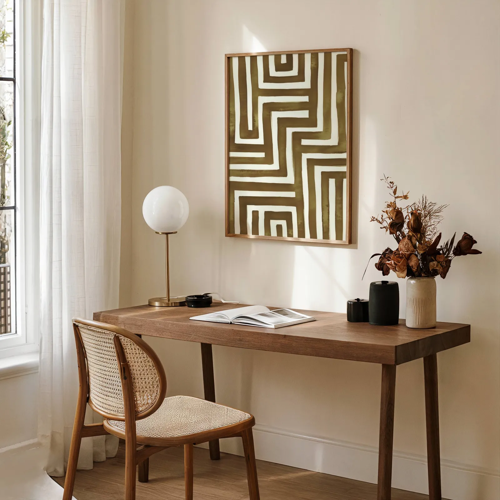 brown abstract maze wall art, above a wooden desk with a globe lamp and dried flowers
