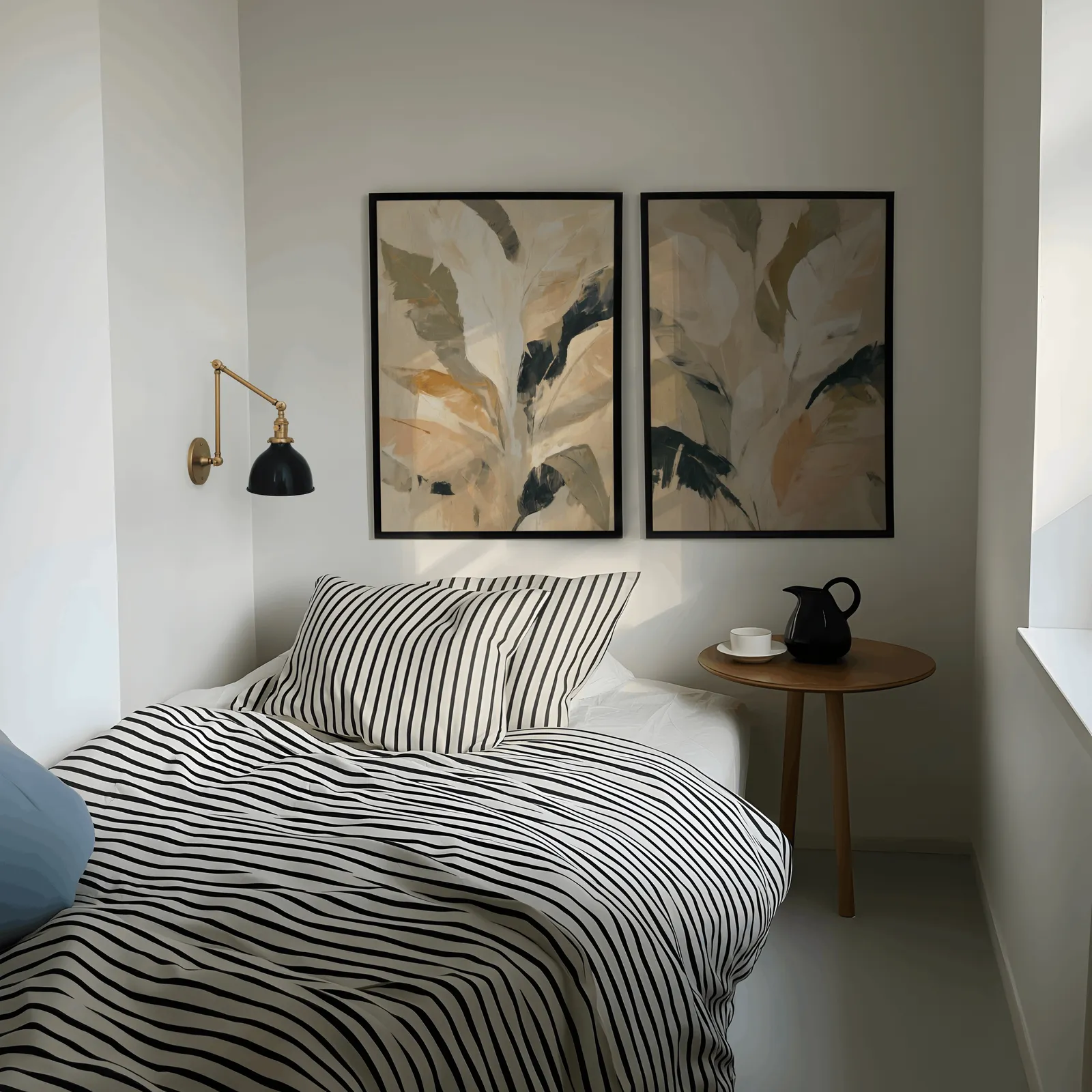 beige botanical leaves wall art set of 2, above a striped bed beside a brass swing-arm lamp