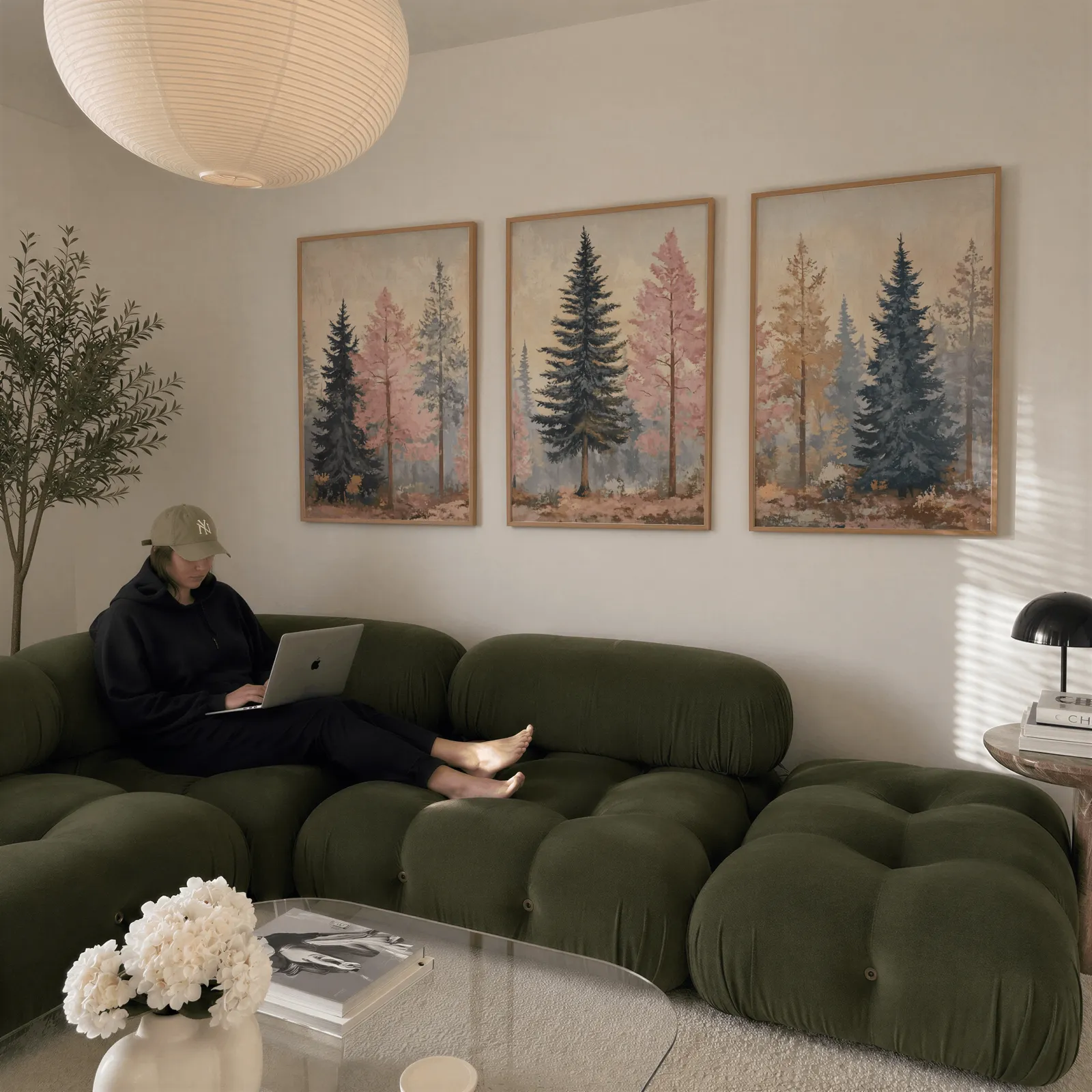 pink and blue pine tree wall art set of 3, above a plush olive velvet sectional beneath a paper lantern light