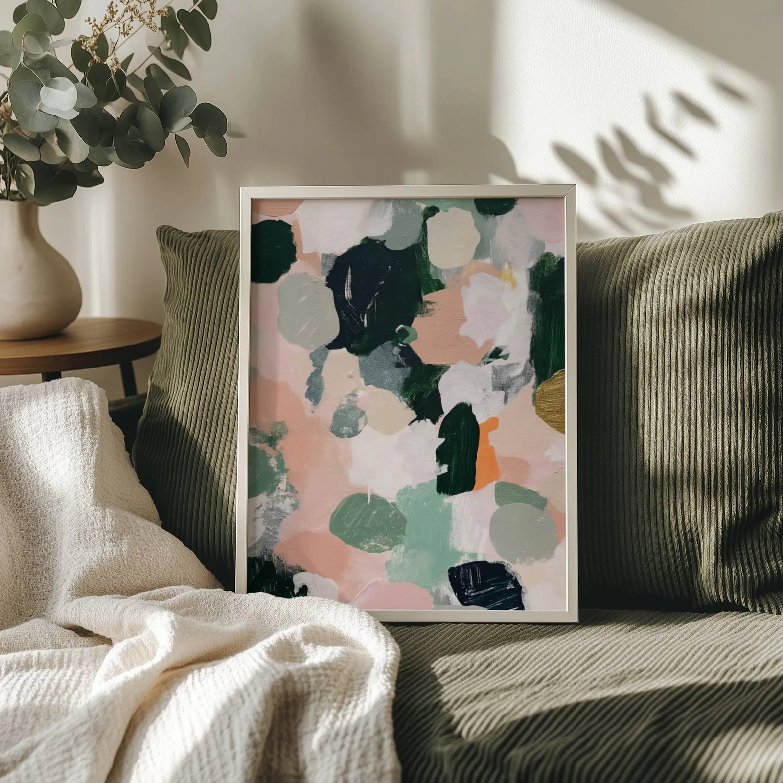 pink and green abstract floral wall art, propped on an olive corduroy sofa beside a eucalyptus vase
