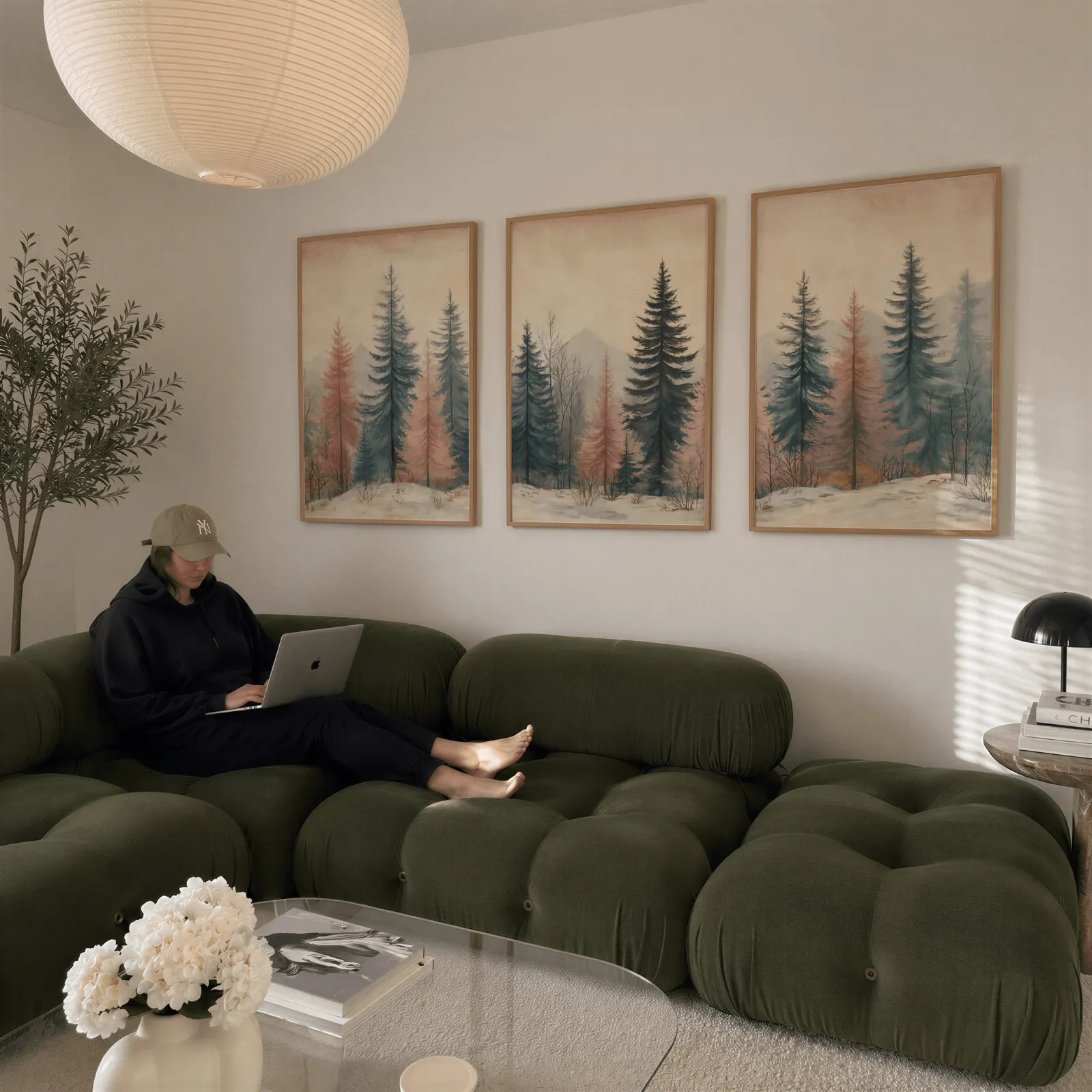 blue and pink pine forest triptych wall art, above a plush olive velvet sectional beneath a paper lantern light