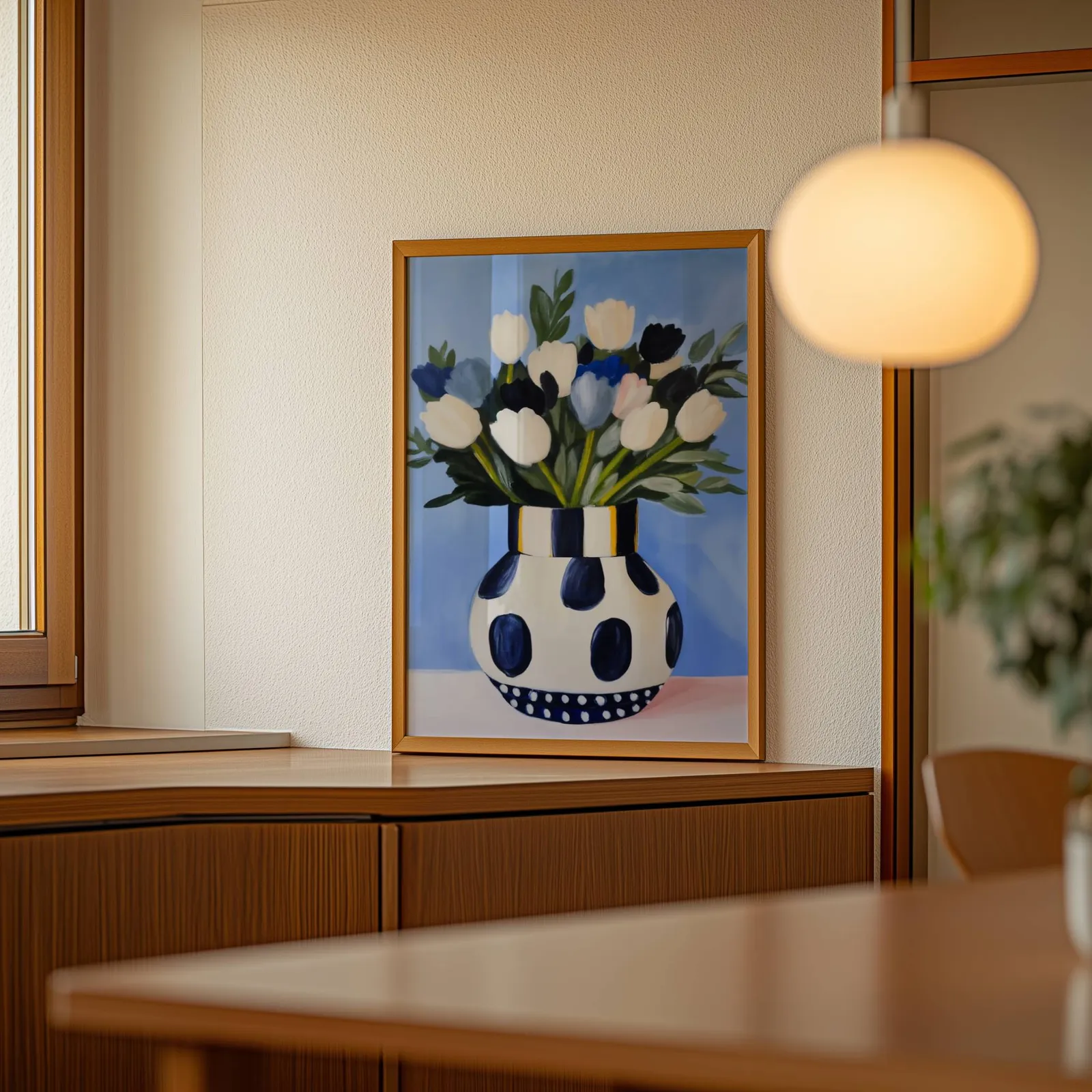 blue floral wall art with polka dot vase, leaning on a wooden sideboard beside a glowing globe pendant