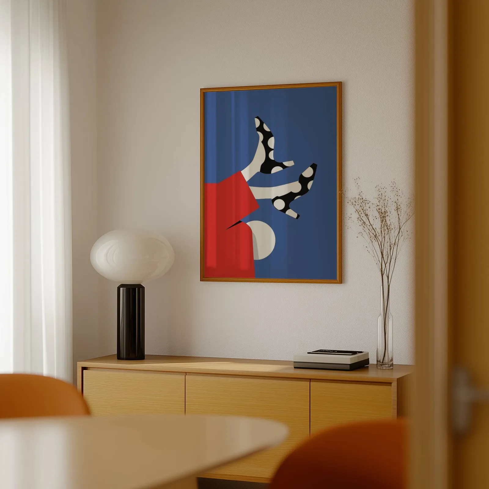playful abstract woman wall art in red and blue, above a light wood sideboard beside a bulbous black lamp