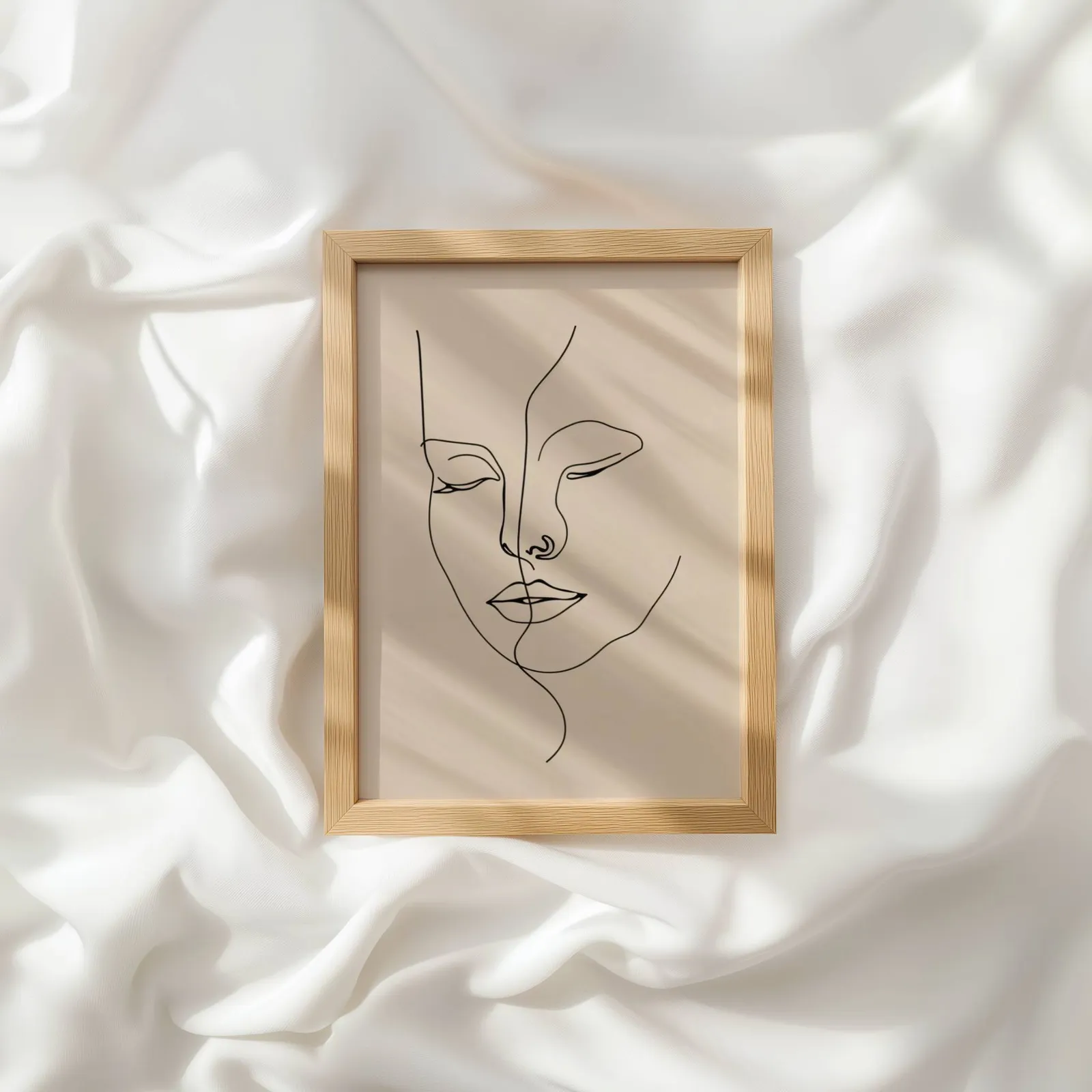 beige abstract face line art wall art, resting atop rumpled white silky fabric