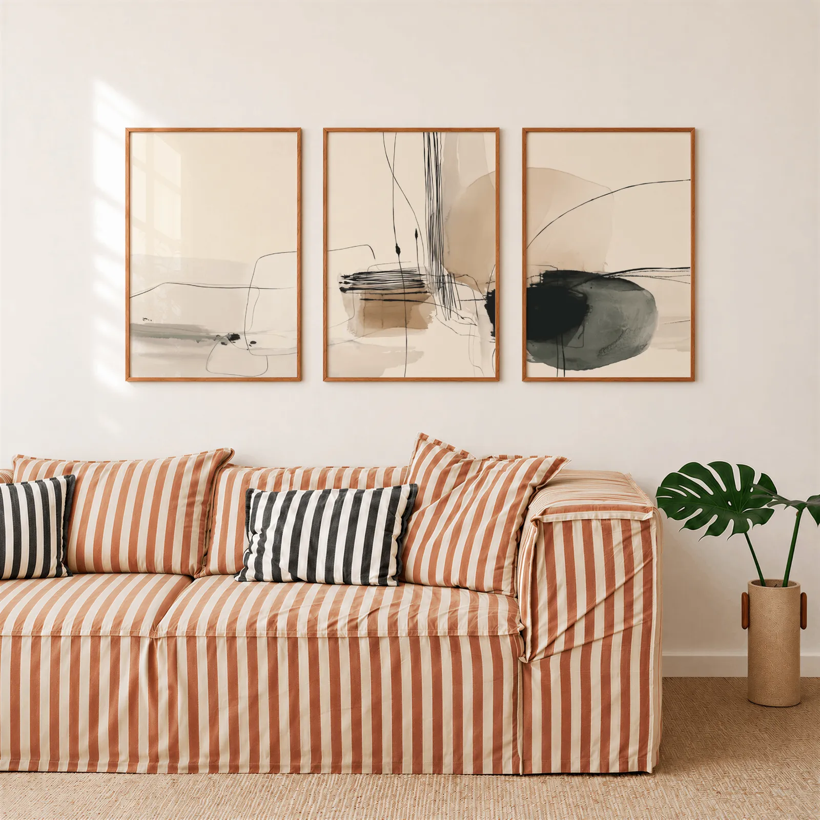 neutral abstract minimalist wall art set of three, above a rust-striped sofa beside a potted monstera
