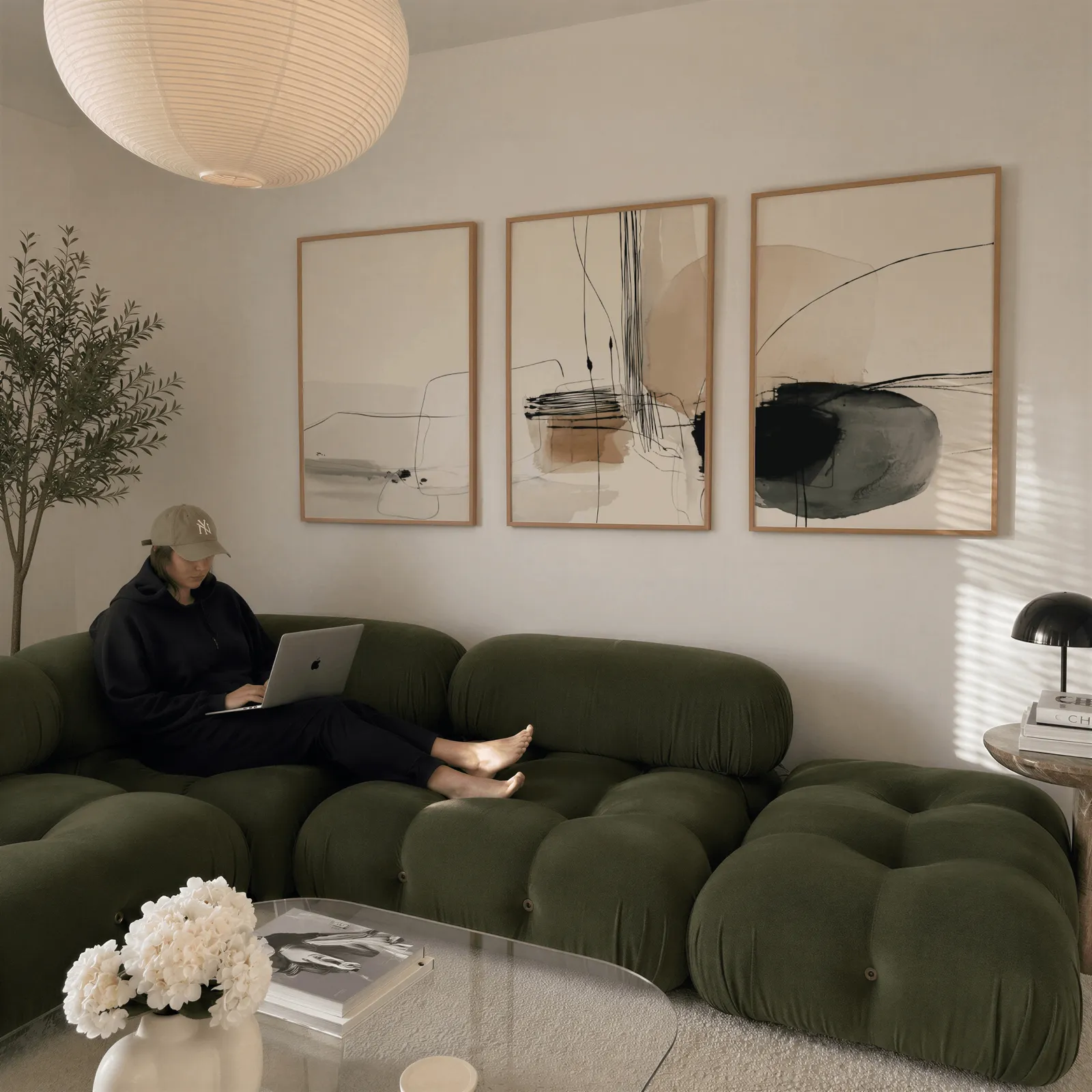 neutral abstract minimalist wall art set of three, above a plush olive velvet sectional beneath a paper lantern light