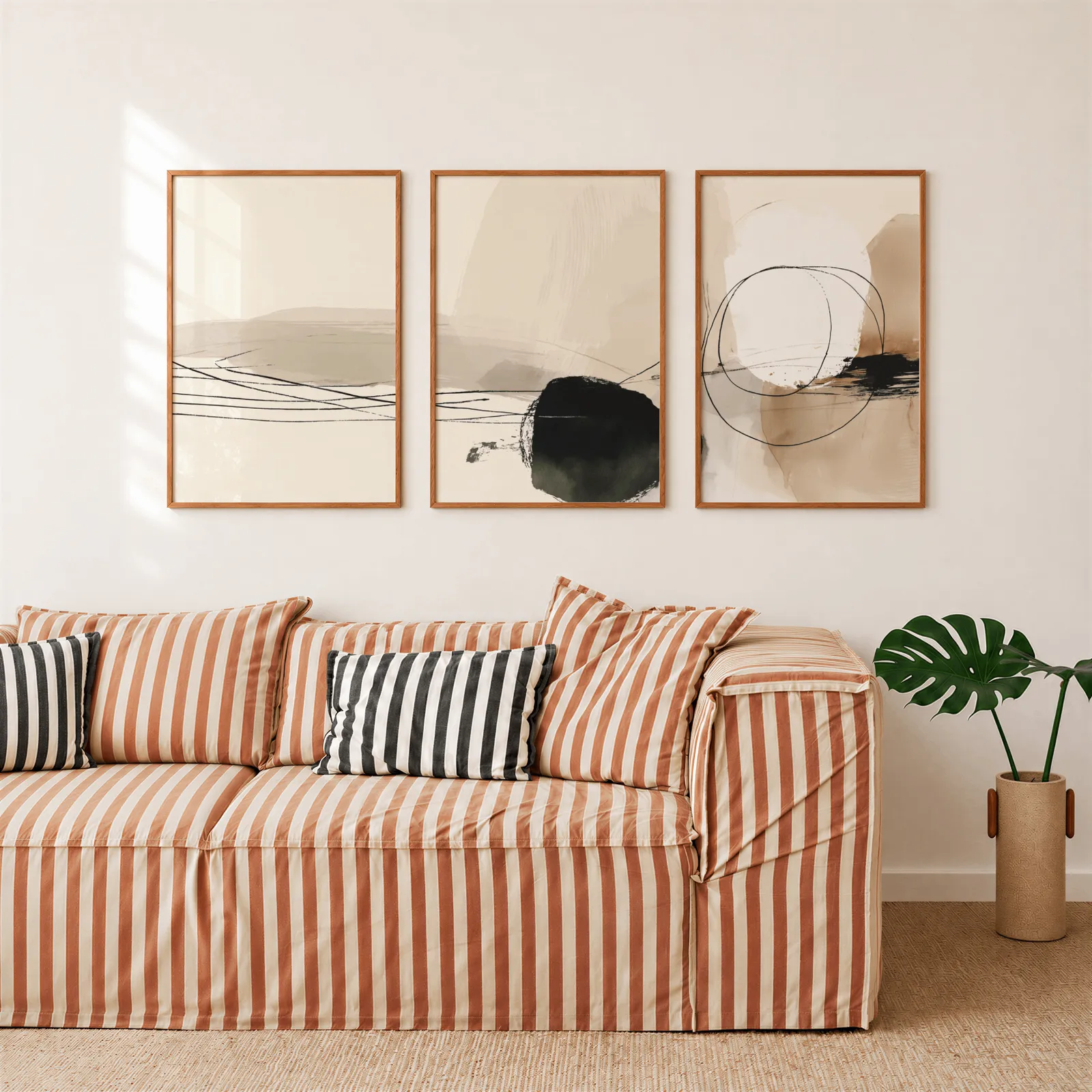 neutral abstract minimalist triptych wall art, above a rust-striped sofa beside a potted monstera