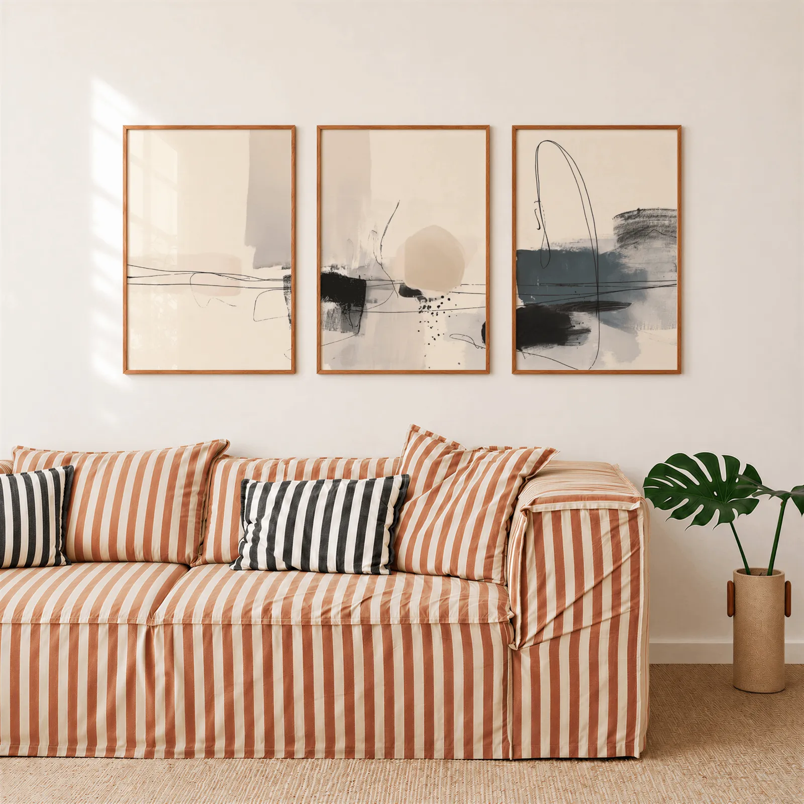 neutral abstract minimalist wall art set of three, above a rust-striped sofa beside a potted monstera