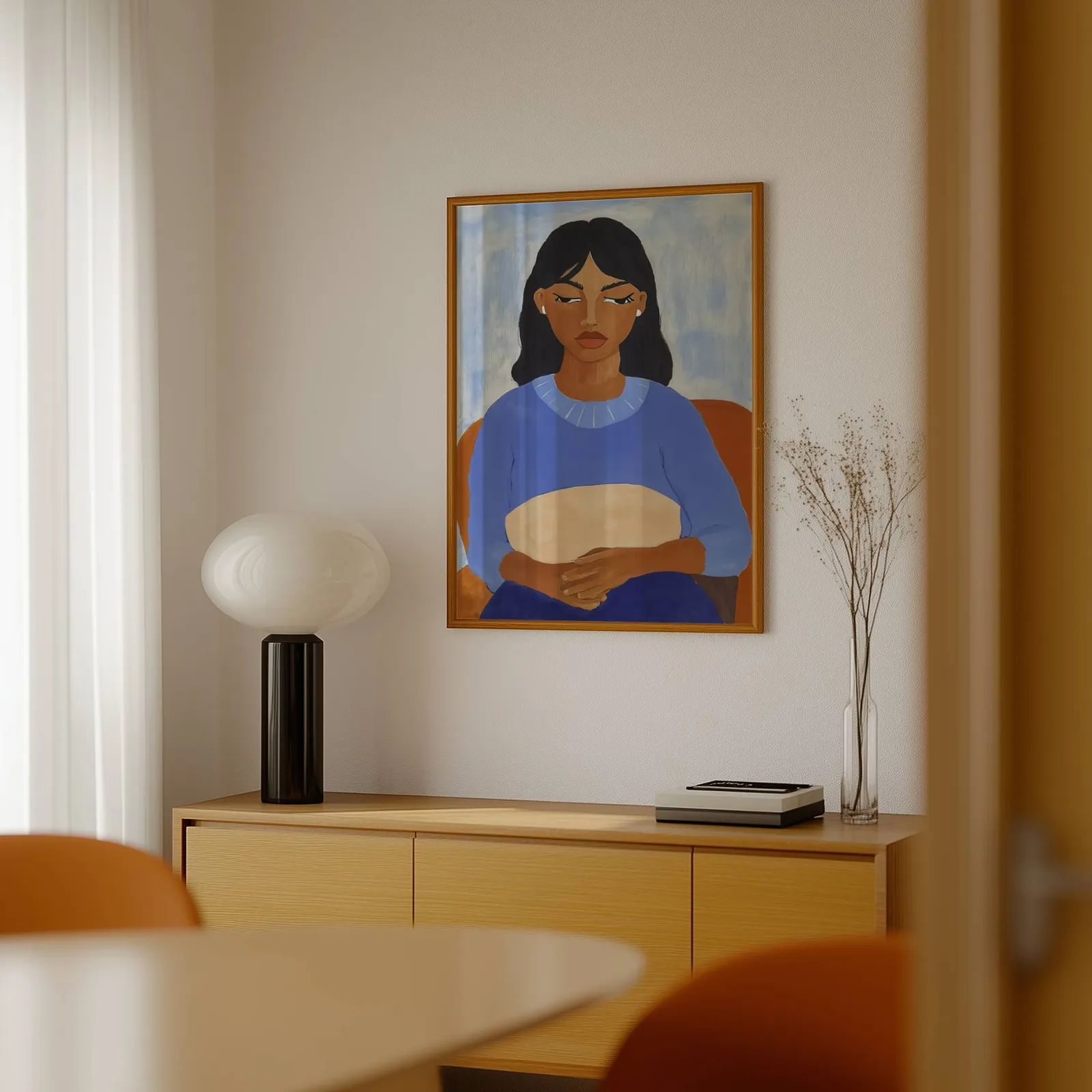blue portrait wall art of seated woman, above a light wood sideboard beside a bulbous black lamp