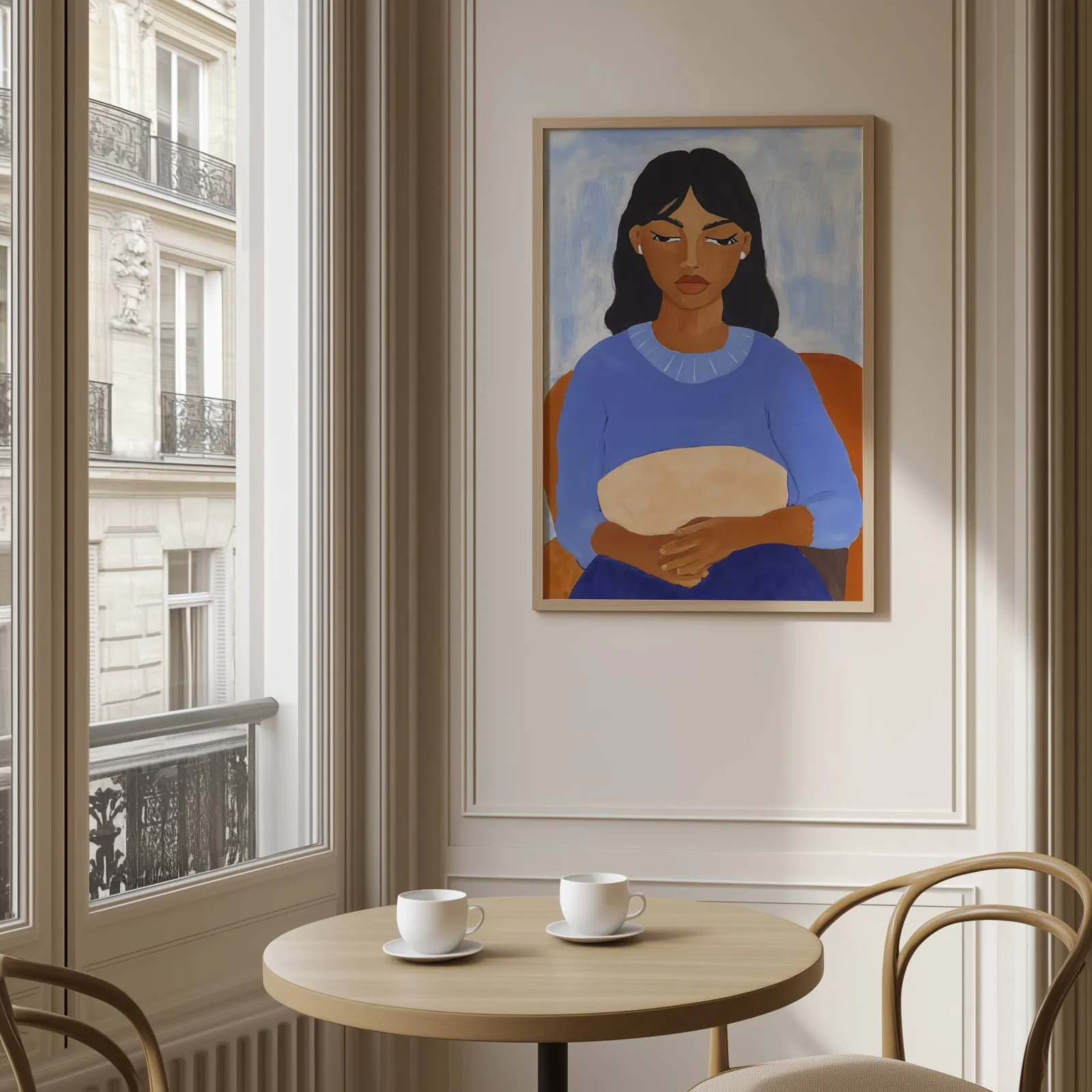 blue portrait wall art of seated woman, above a round café table set with two coffee cups