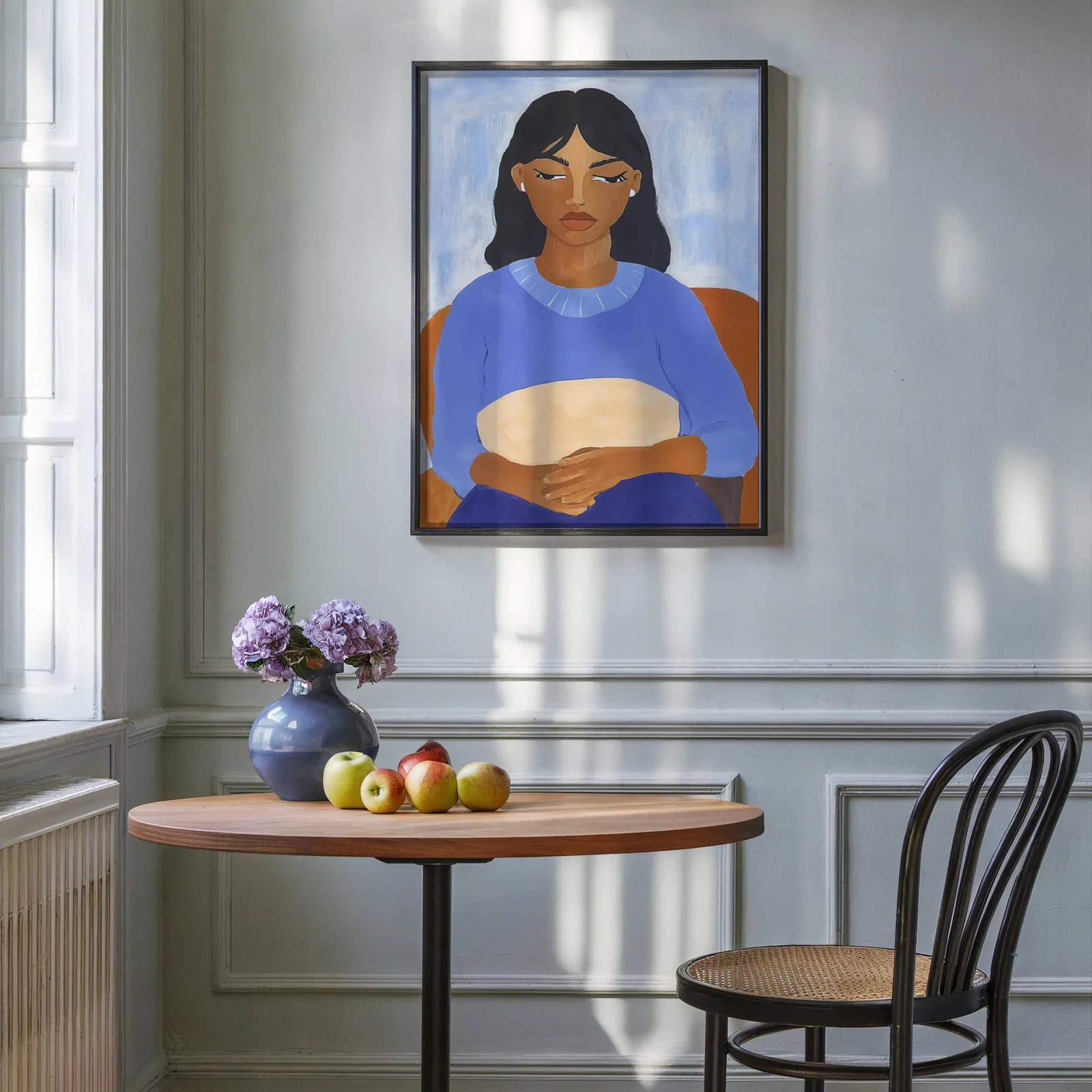 blue portrait wall art of seated woman, above a round wooden table with apples and a blue vase