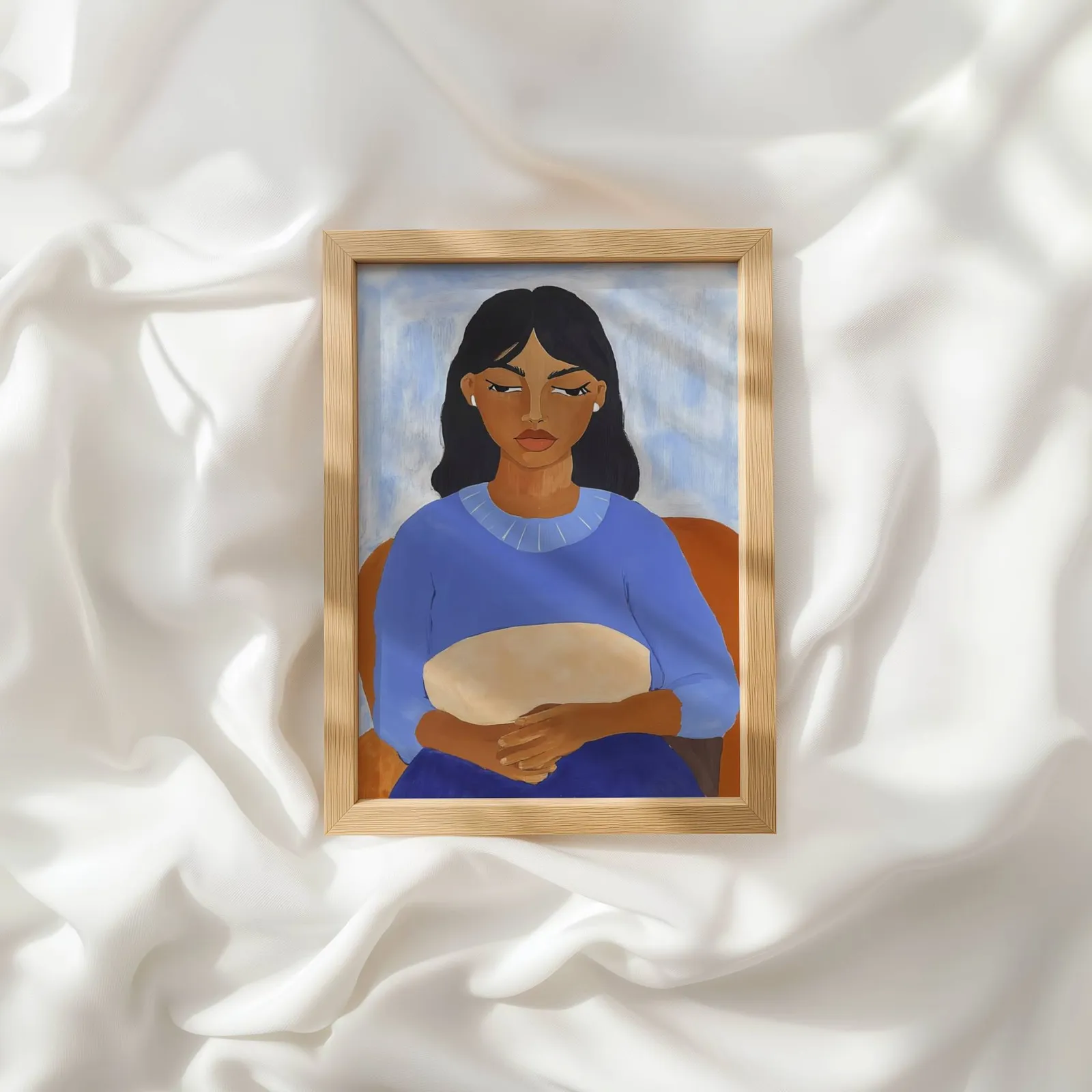 blue portrait wall art of seated woman, resting atop rumpled white silky fabric