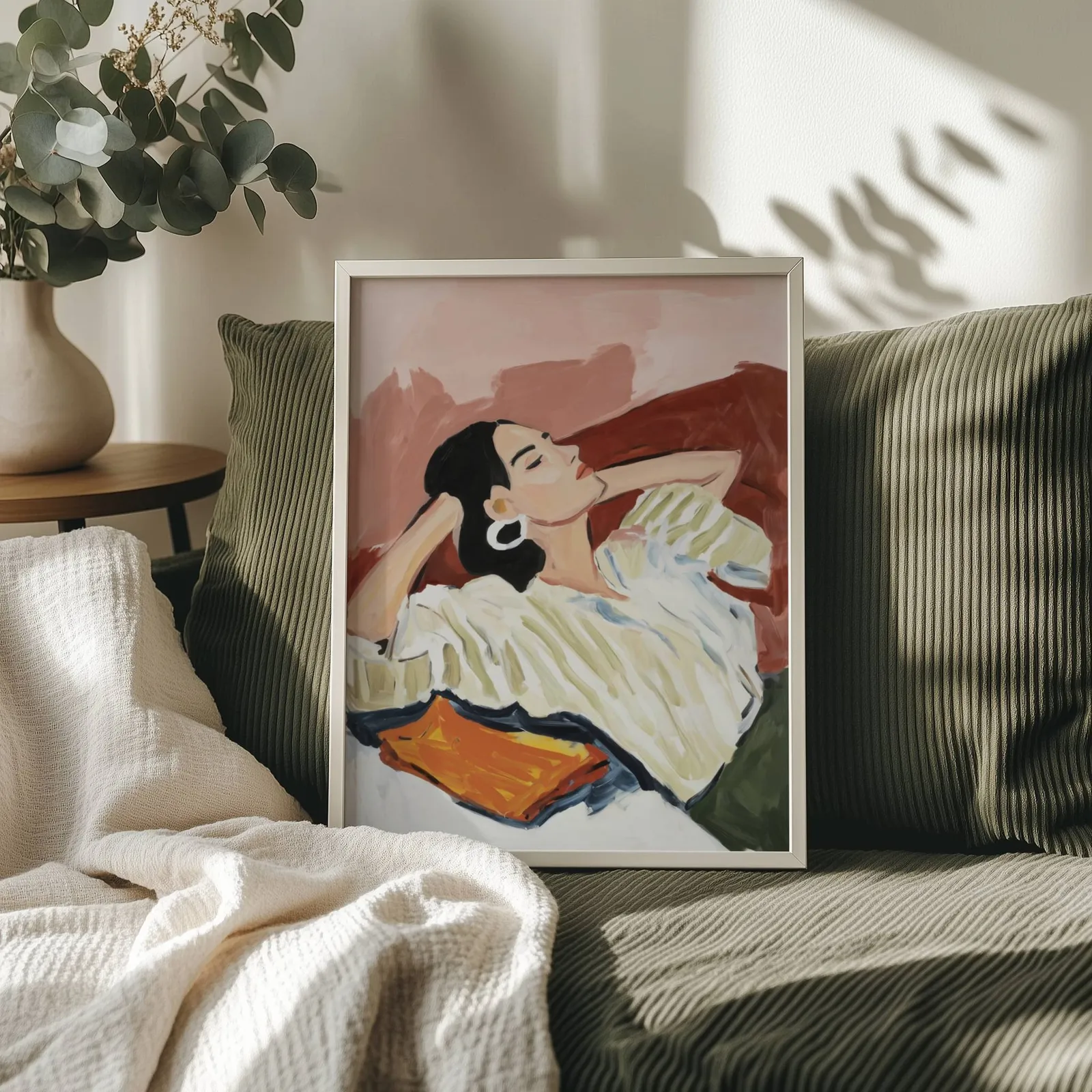 terracotta reclining woman portrait wall art, propped on an olive corduroy sofa beside a eucalyptus vase