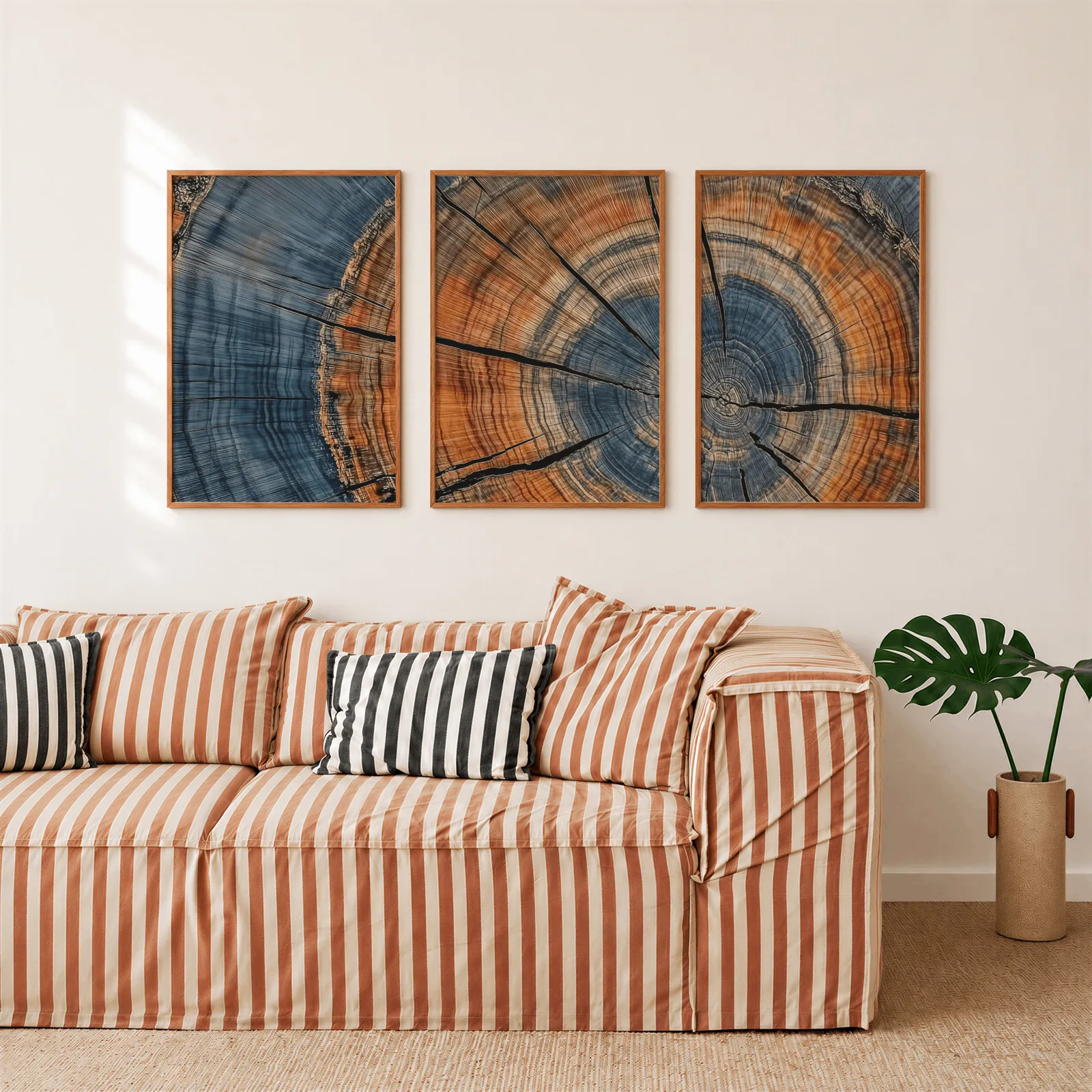 blue and orange tree rings triptych wall art, above a rust-striped sofa beside a potted monstera