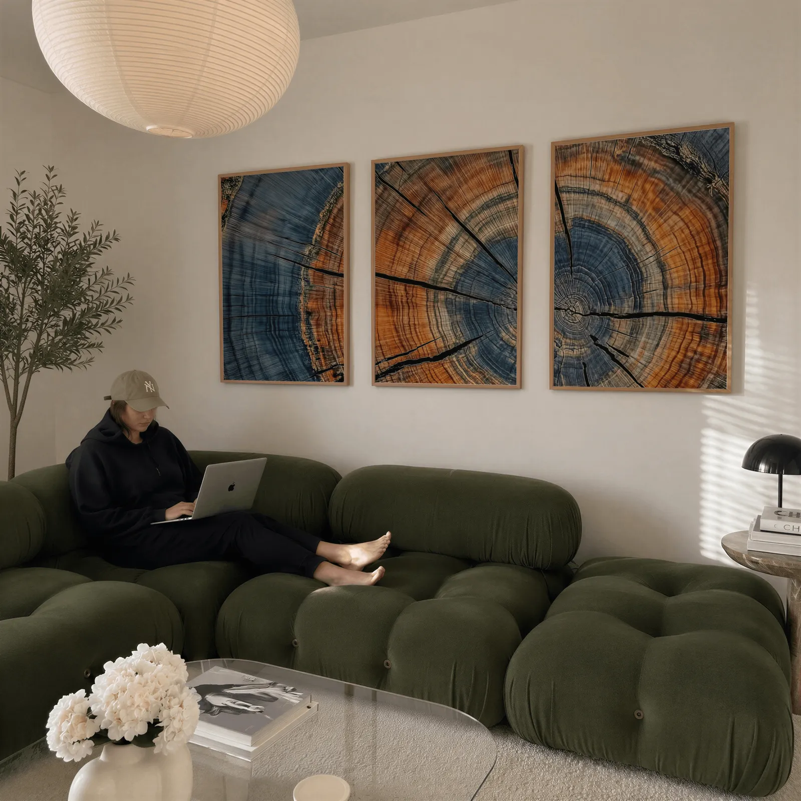 blue and orange tree rings triptych wall art, above a plush olive velvet sectional beneath a paper lantern light