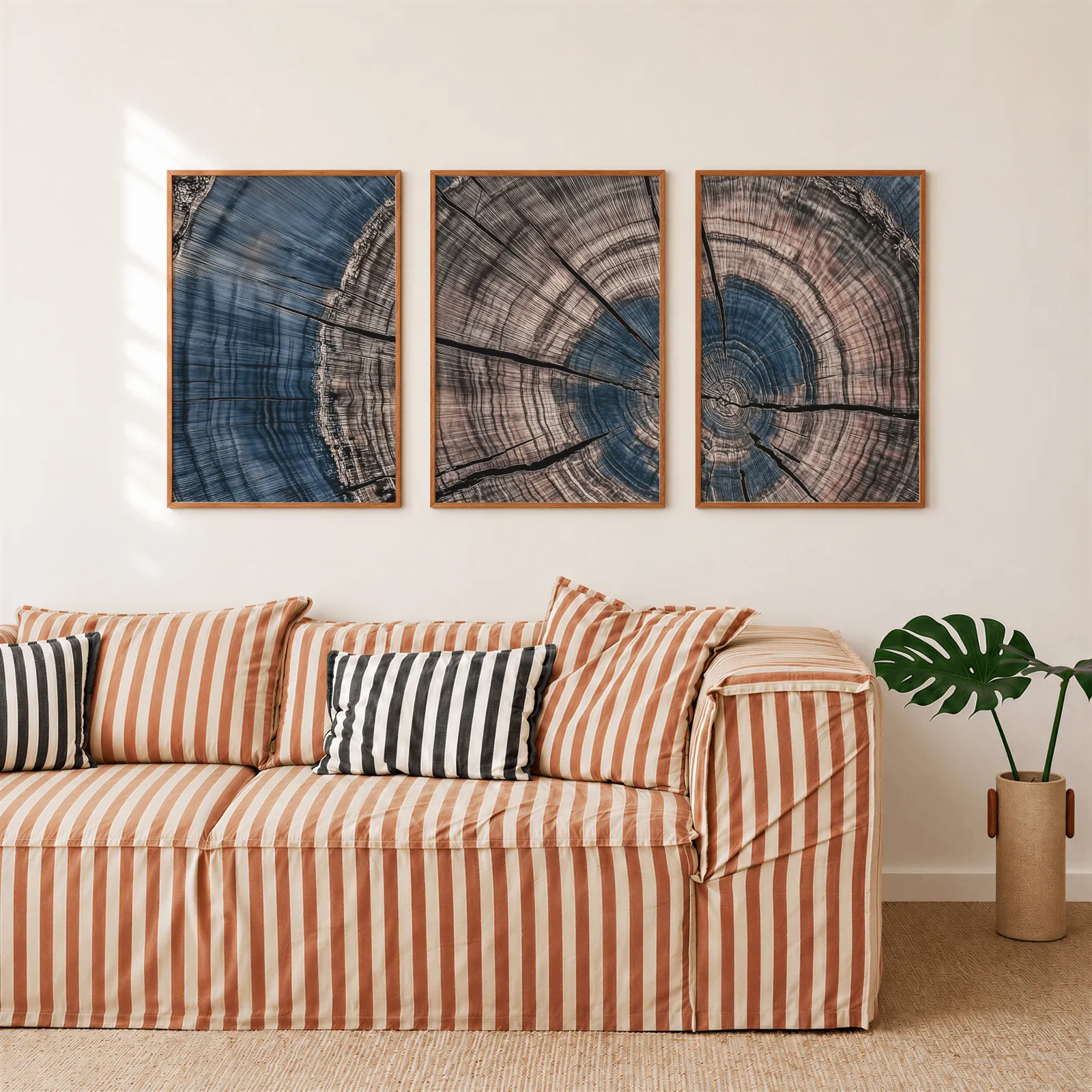 blue and pink tree rings triptych wall art, above a rust-striped sofa beside a potted monstera