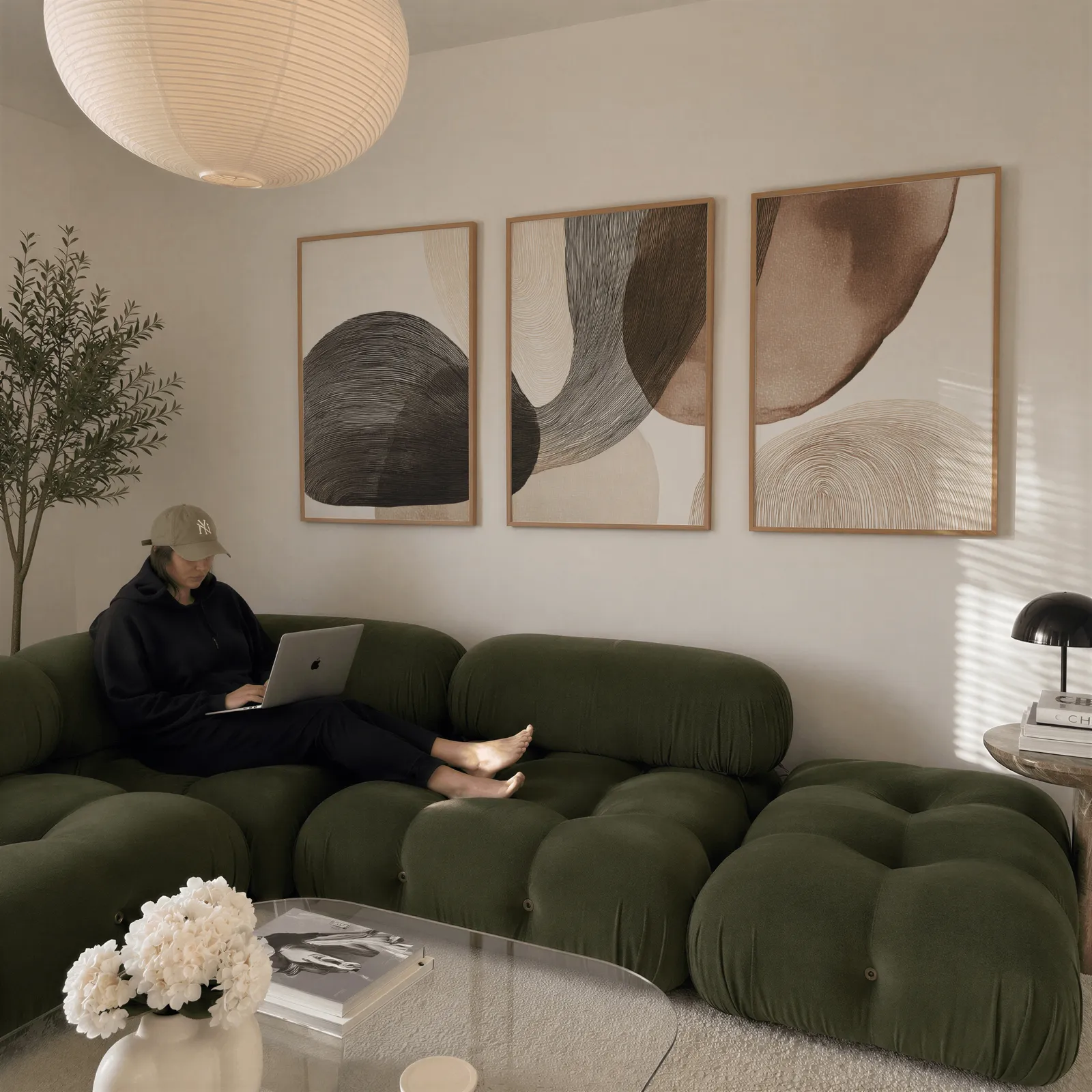 neutral abstract wall art set of 3 with curved organic forms, above a plush olive velvet sectional beneath a paper lantern light