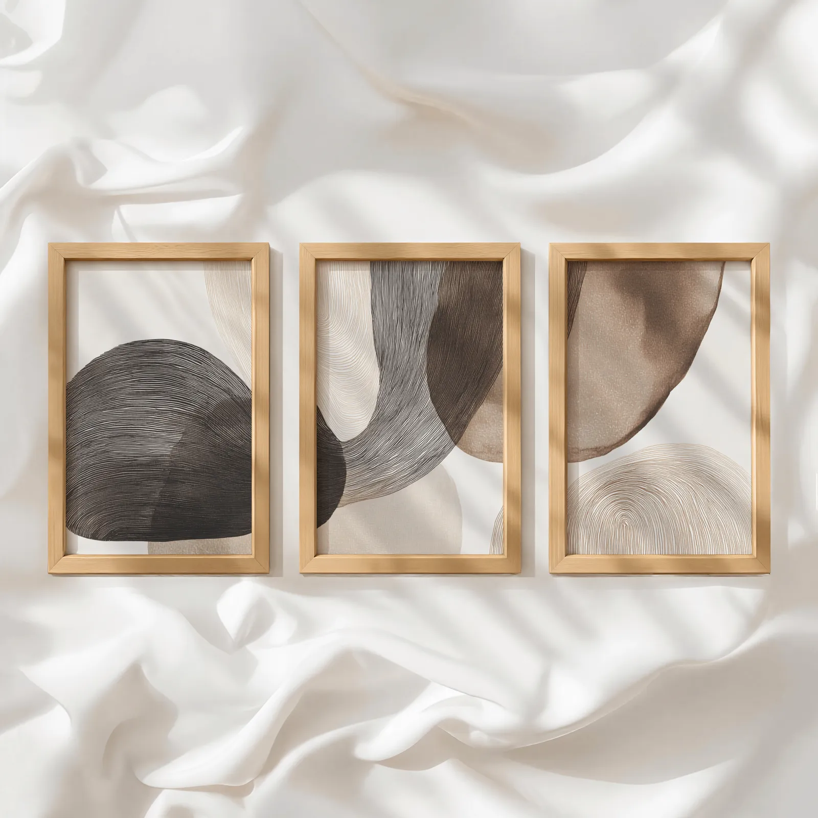 neutral abstract wall art set of 3 with curved organic forms, in a row atop rumpled white silky fabric