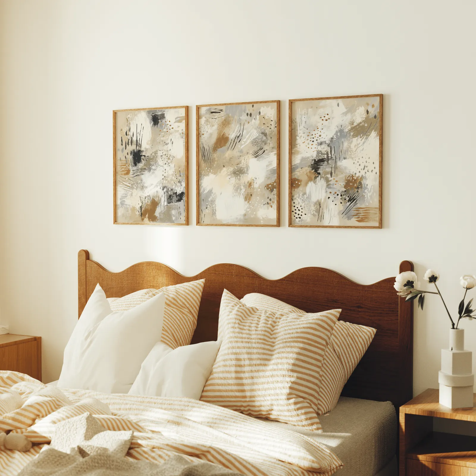 neutral abstract three piece wall art in beige and black, above a scalloped wooden headboard with striped pillows