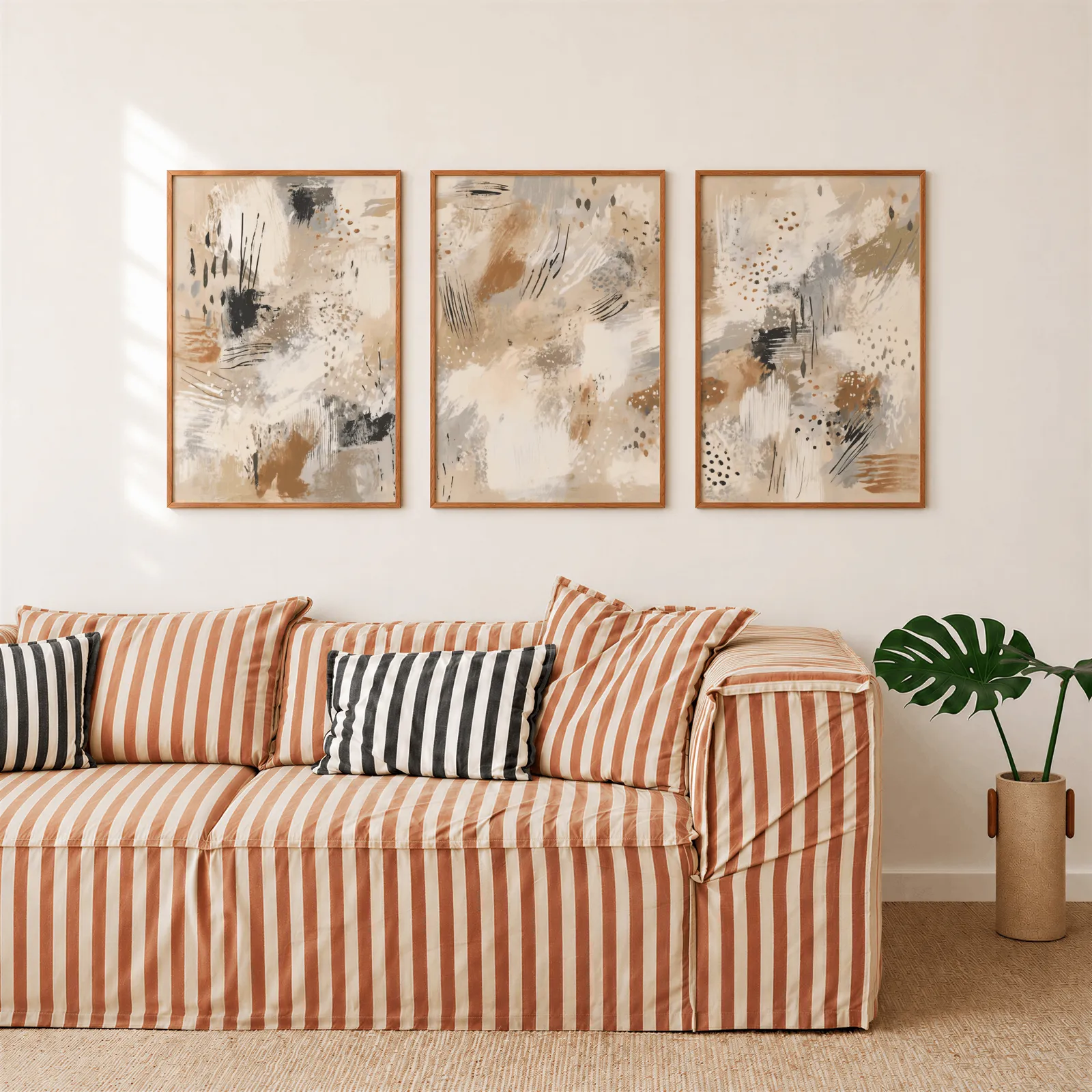 neutral abstract three piece wall art in beige and black, above a rust-striped sofa beside a potted monstera