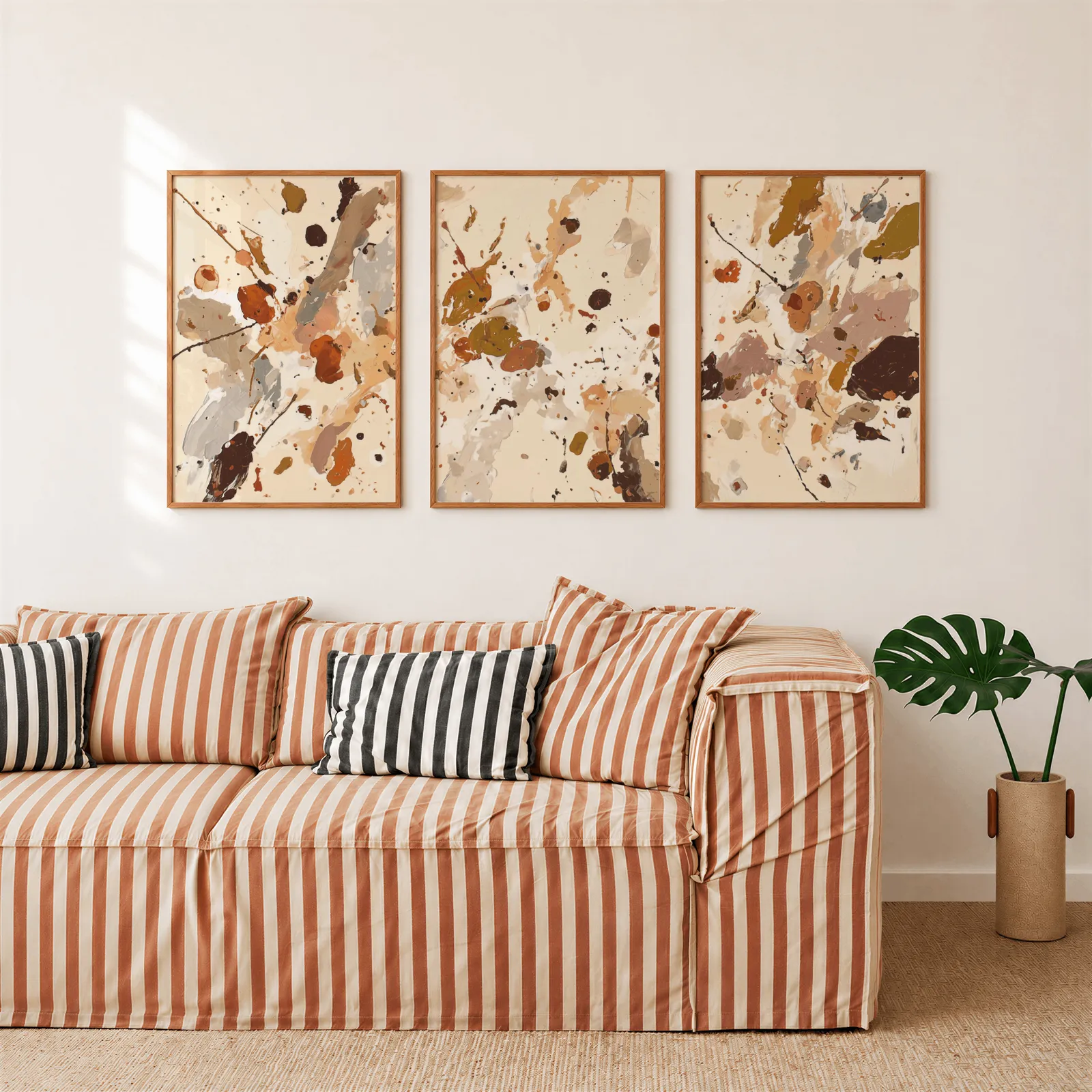 terracotta abstract splatter wall art set of 3, above a rust-striped sofa beside a potted monstera