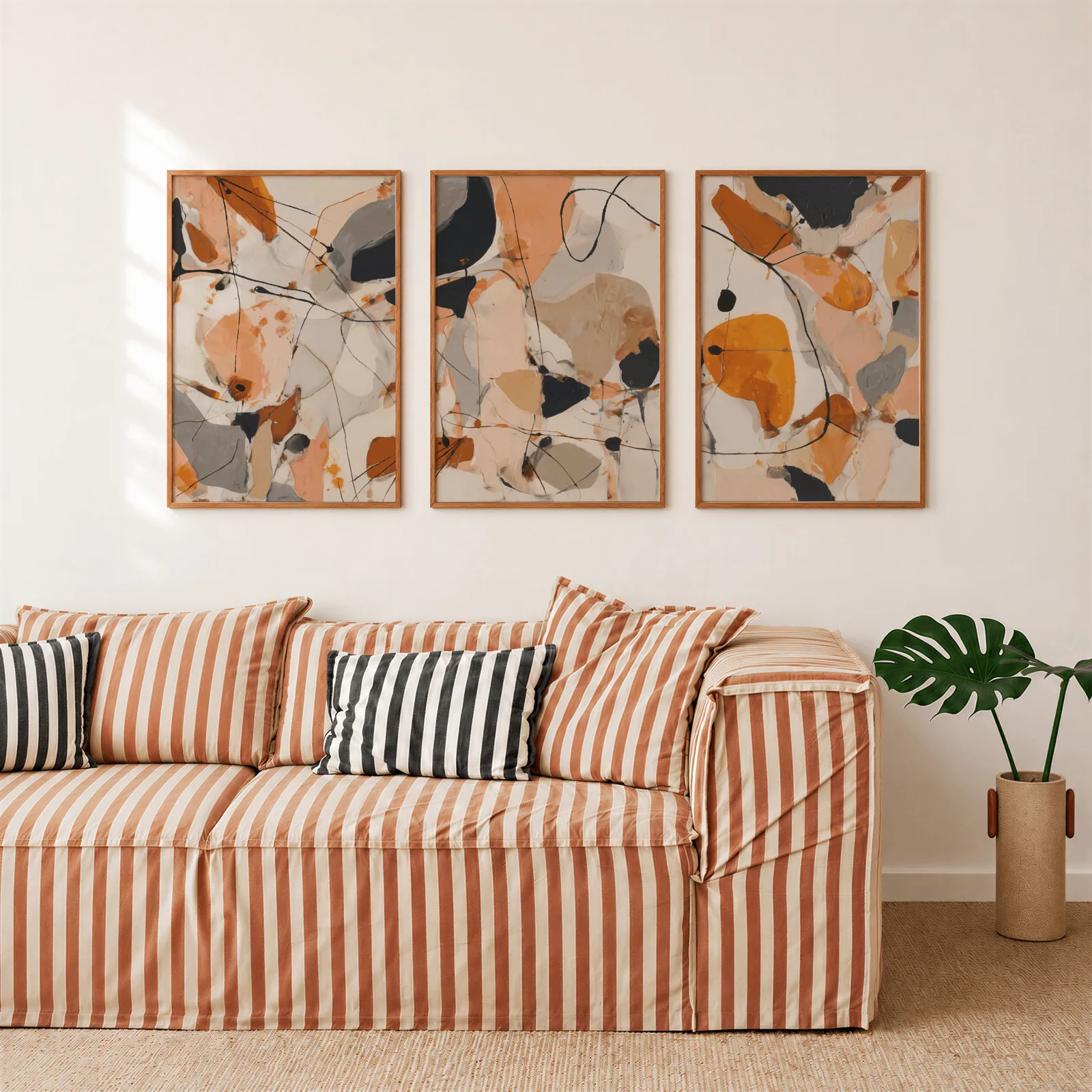orange abstract triptych wall art set, above a rust-striped sofa beside a potted monstera