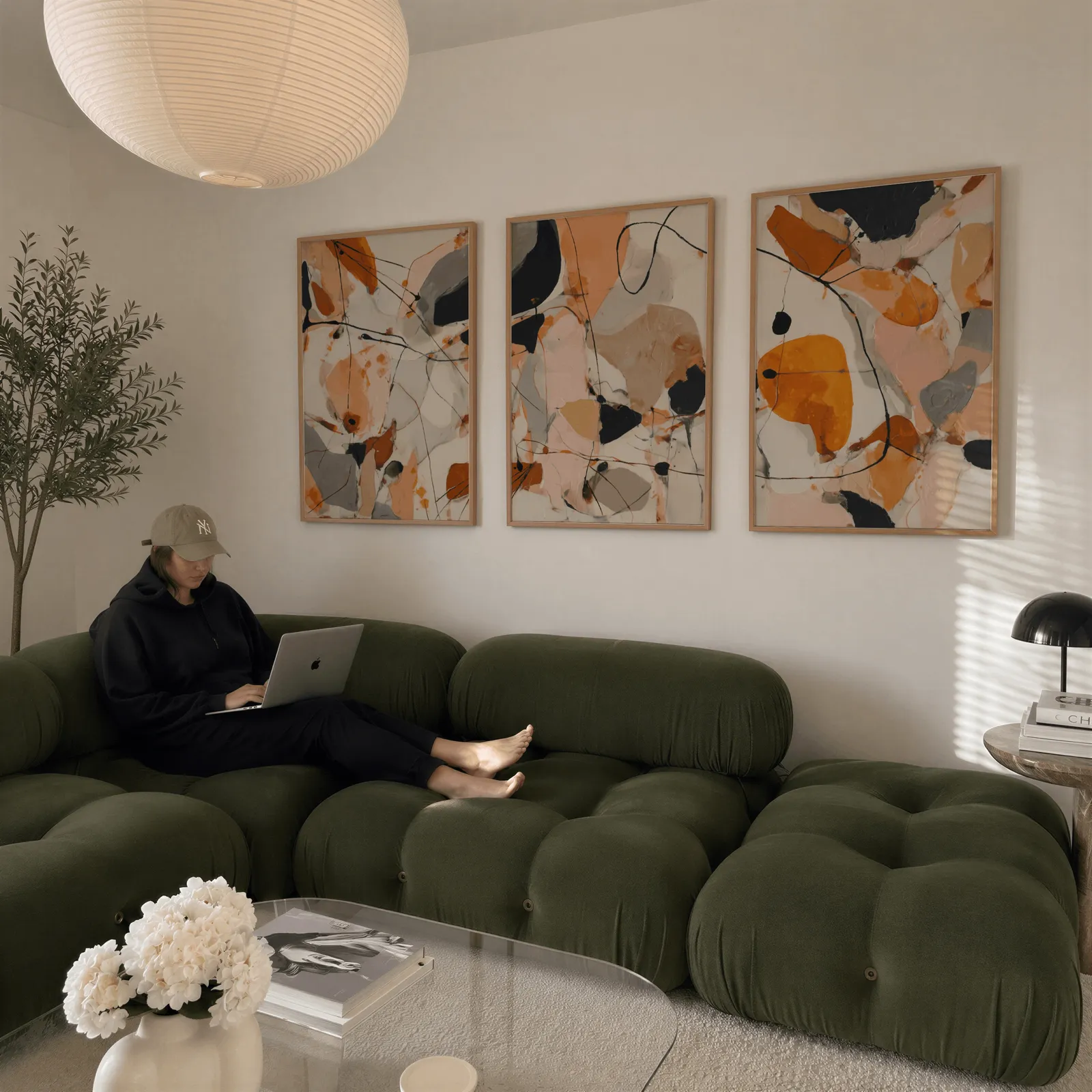 orange abstract triptych wall art set, above a plush olive velvet sectional beneath a paper lantern light