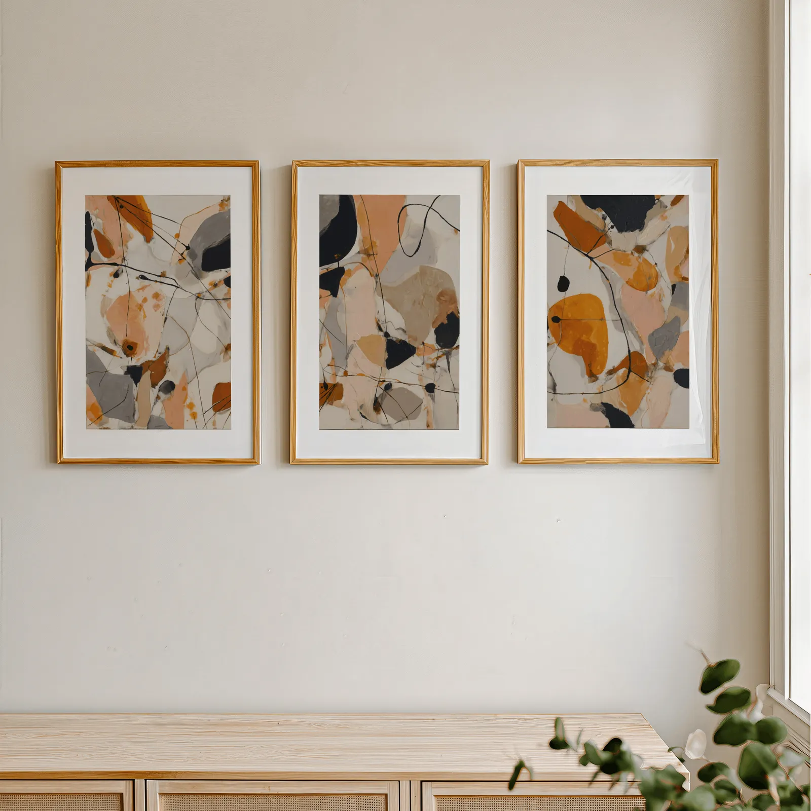 orange abstract triptych wall art set, in a row above a light wooden sideboard near a window