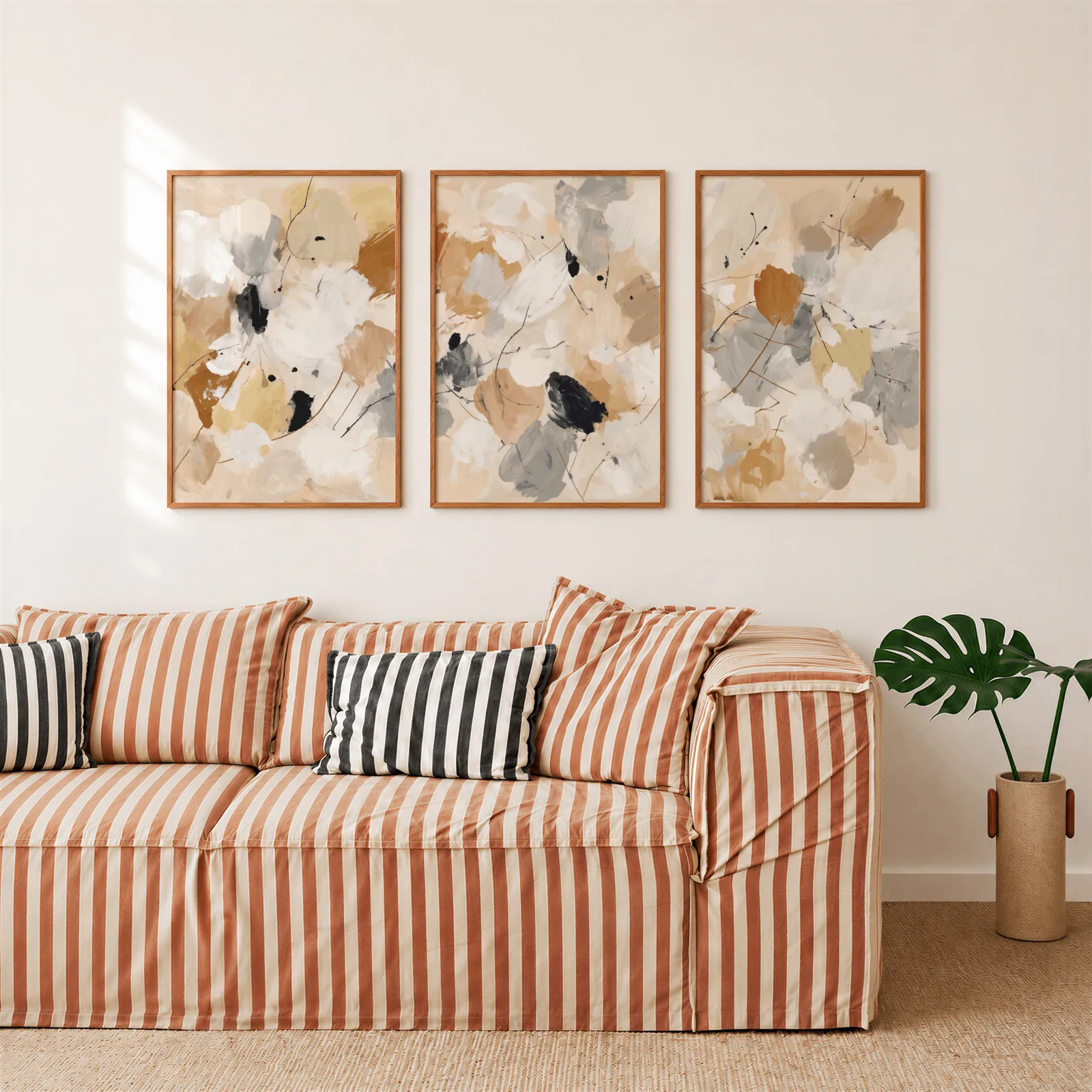 neutral abstract triptych wall art, above a rust-striped sofa beside a potted monstera