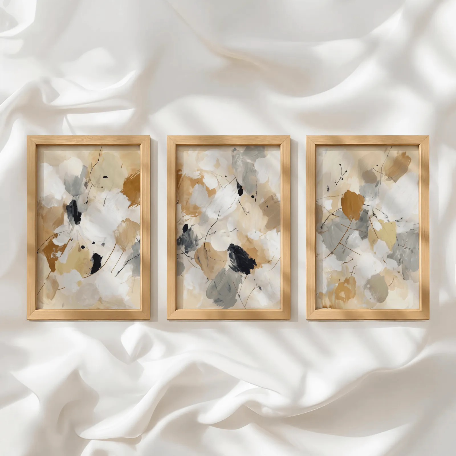neutral abstract triptych wall art, in a row atop rumpled white silky fabric