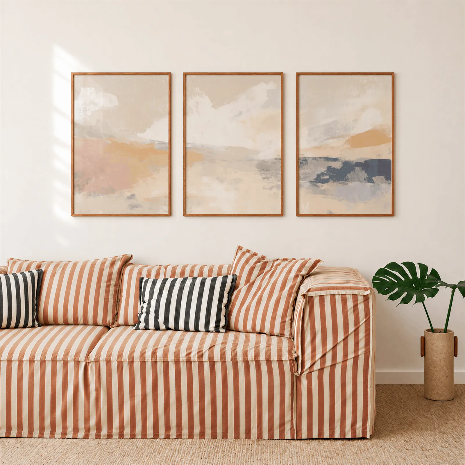 terracotta and blue abstract landscape wall art set of 3, above a rust-striped sofa beside a potted monstera