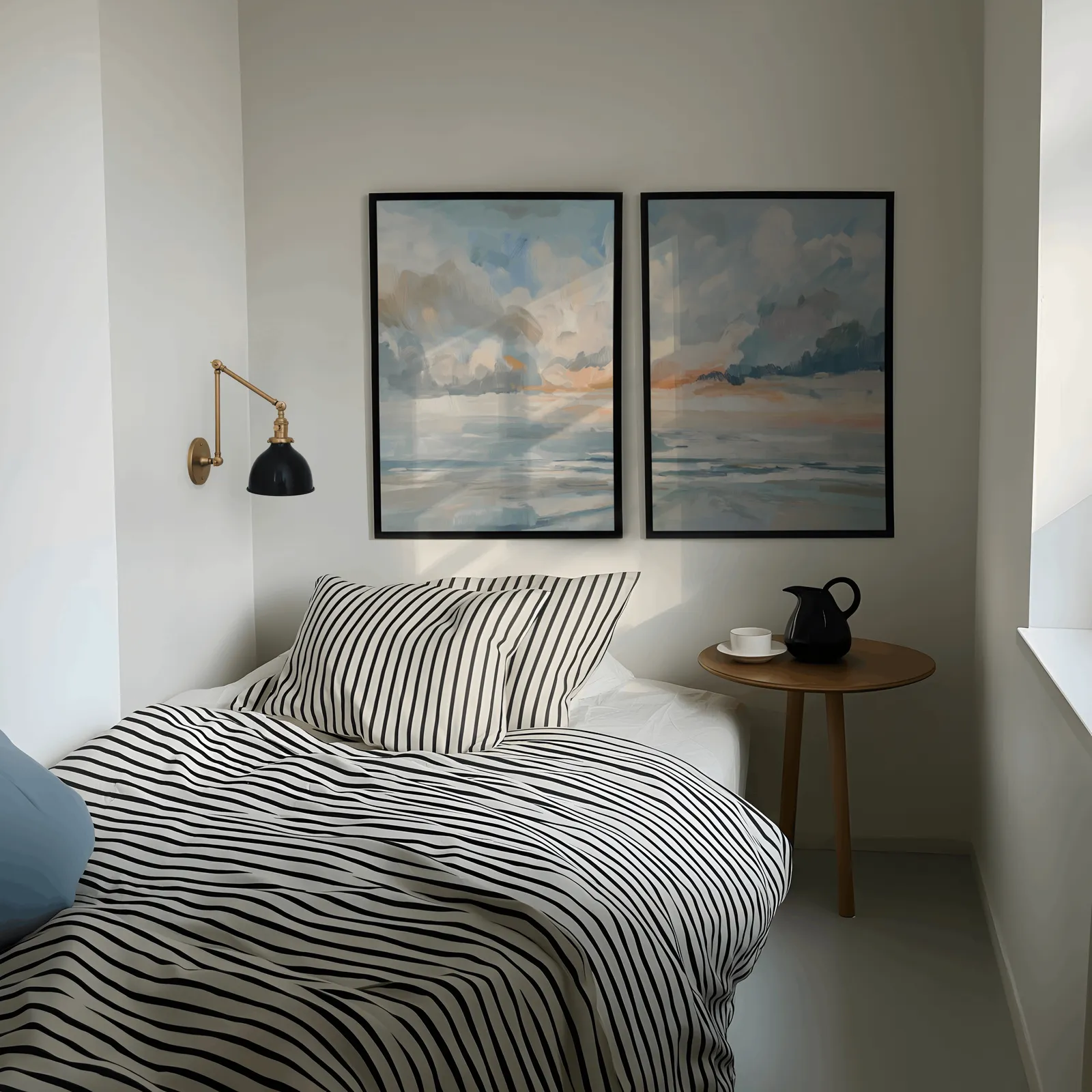blue and orange coastal sky wall art set of two, above a striped bed beside a brass swing-arm lamp