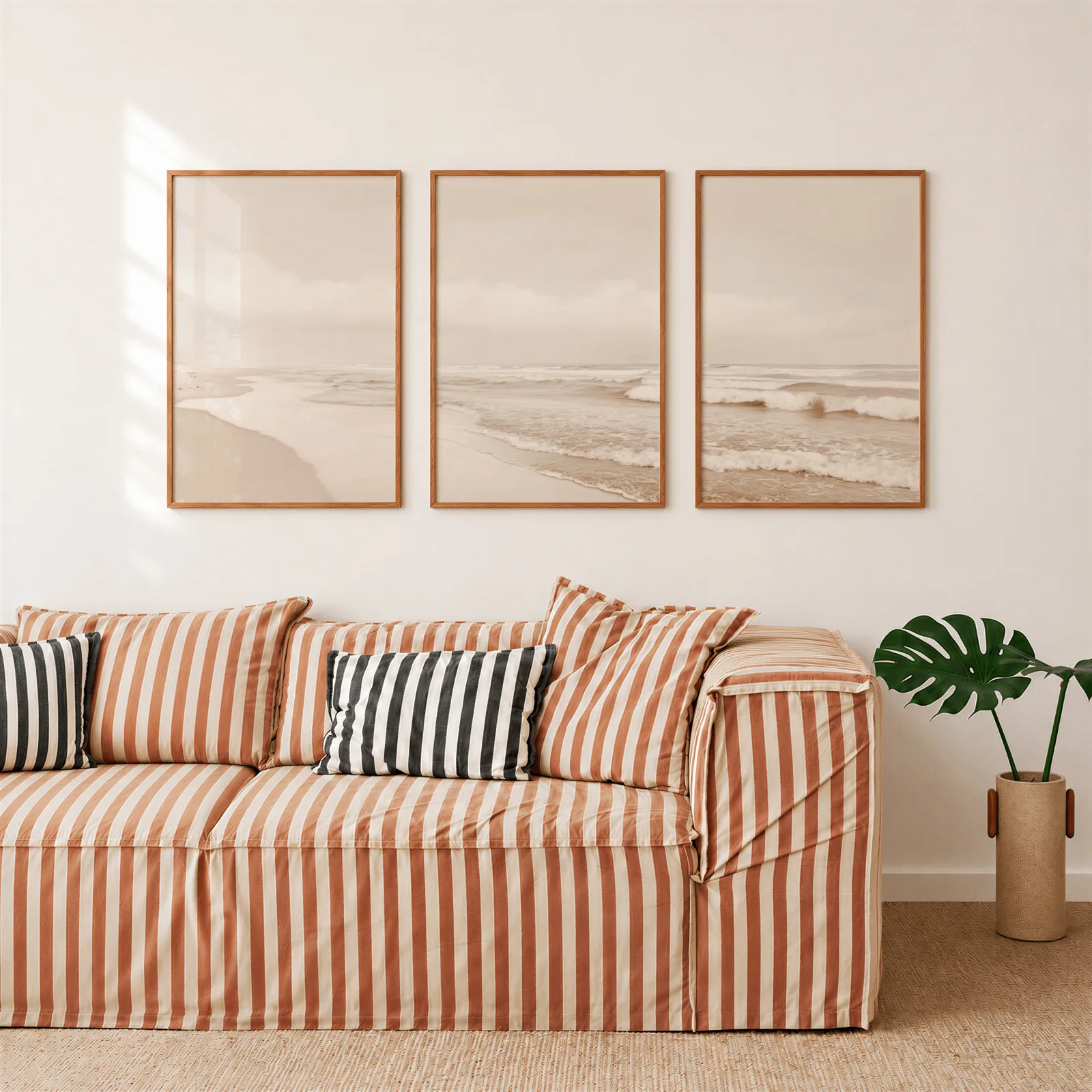 neutral coastal beach triptych wall art, above a rust-striped sofa beside a potted monstera