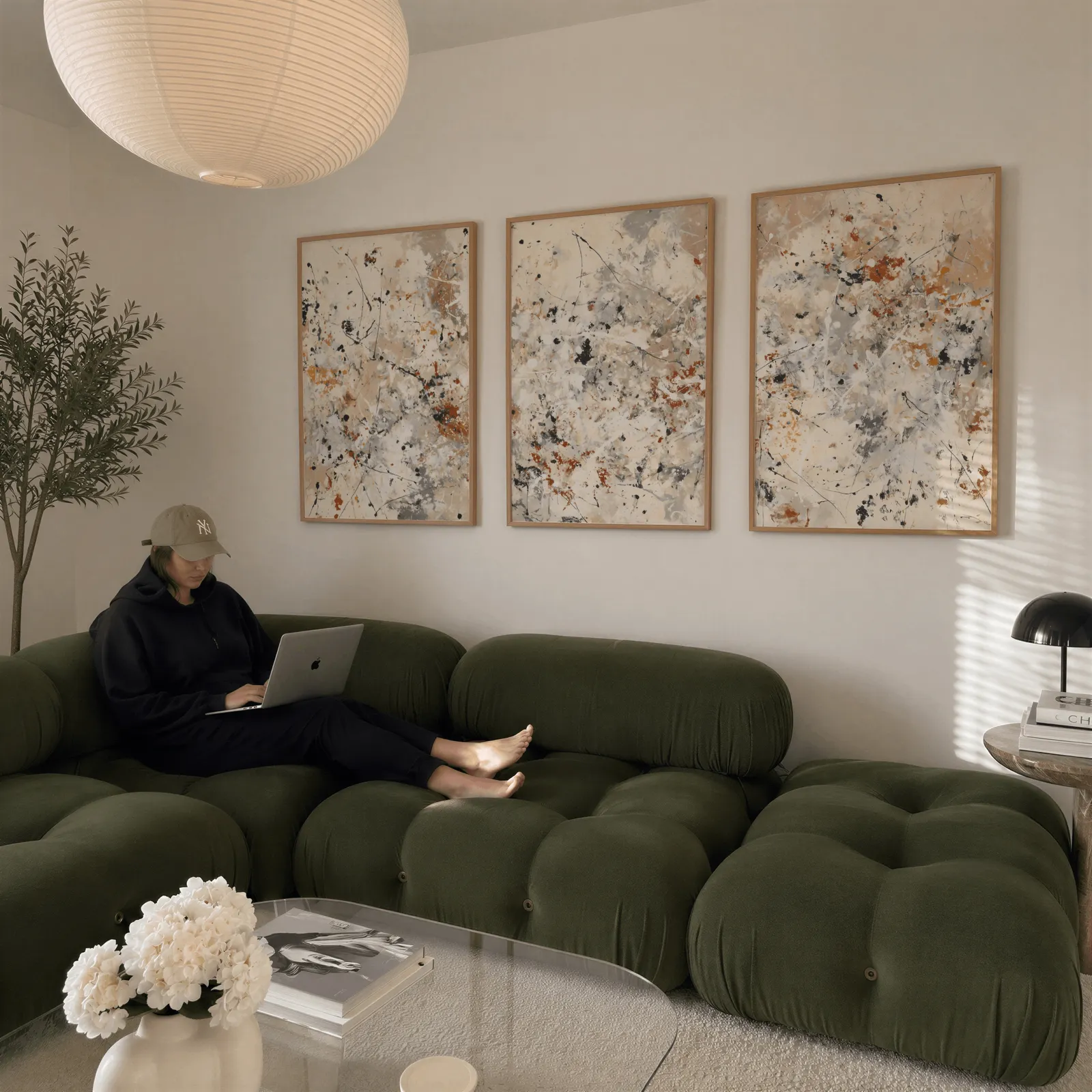 neutral abstract splatter wall art set of three, above a plush olive velvet sectional beneath a paper lantern light