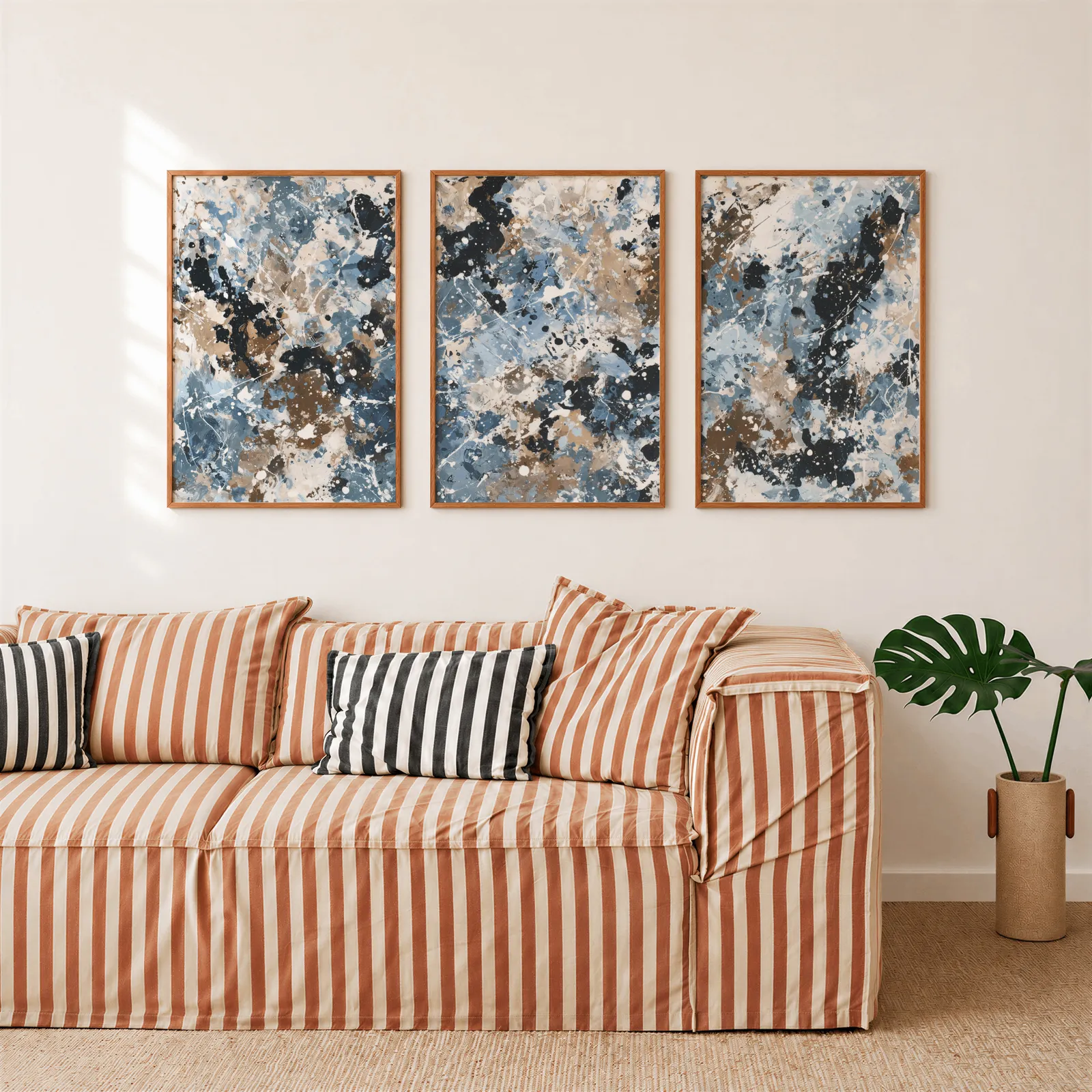 blue brown abstract splatter triptych wall art, above a rust-striped sofa beside a potted monstera