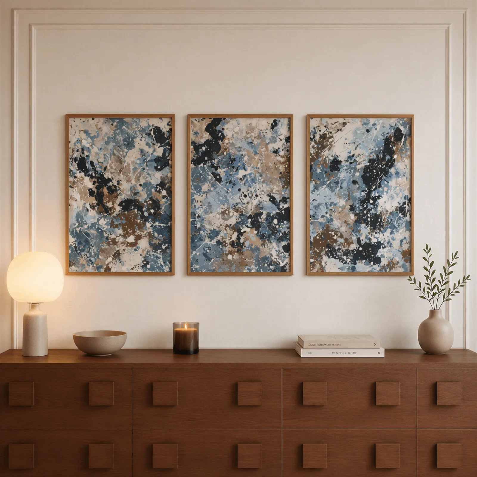 blue brown abstract splatter triptych wall art, above a walnut sideboard with a lit candle and glowing lamp