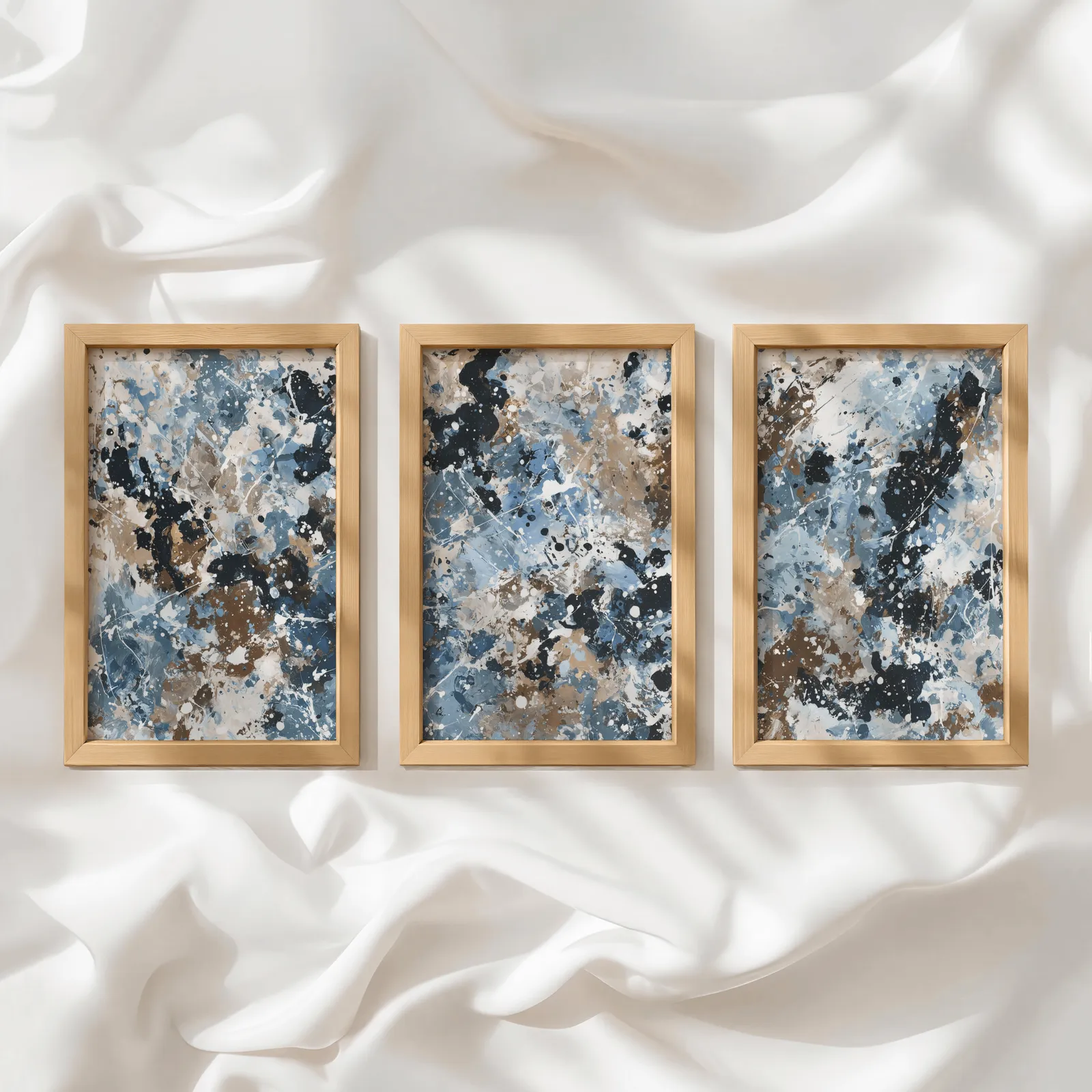 blue brown abstract splatter triptych wall art, in a row atop rumpled white silky fabric