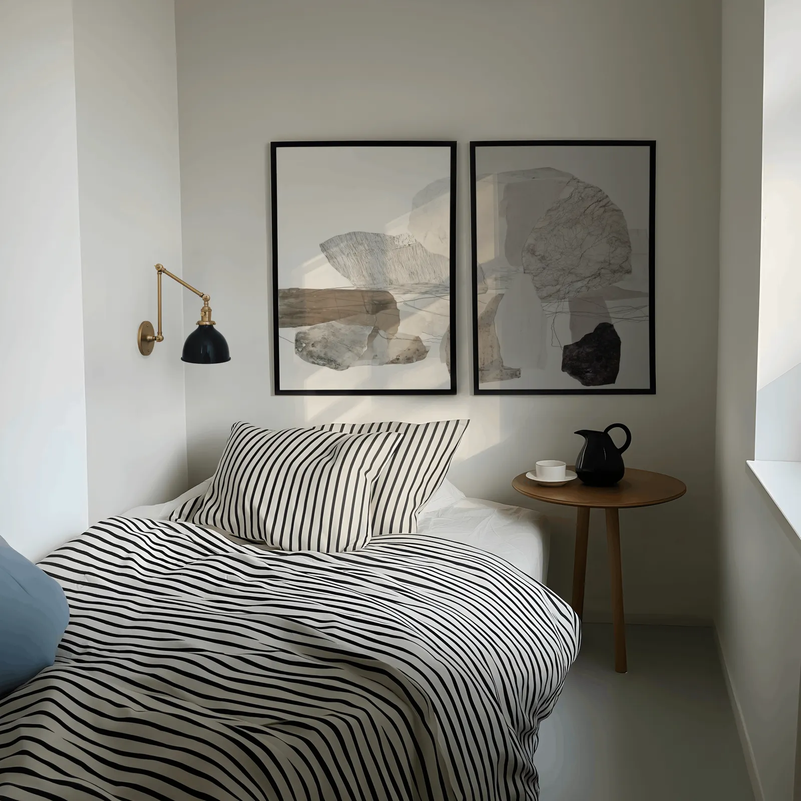 neutral abstract stone wall art set of two, above a striped bed beside a brass swing-arm lamp