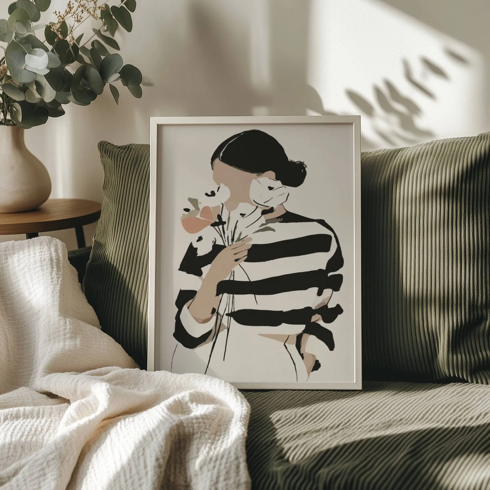 woman with flowers abstract face art print, propped on an olive corduroy sofa beside a eucalyptus vase