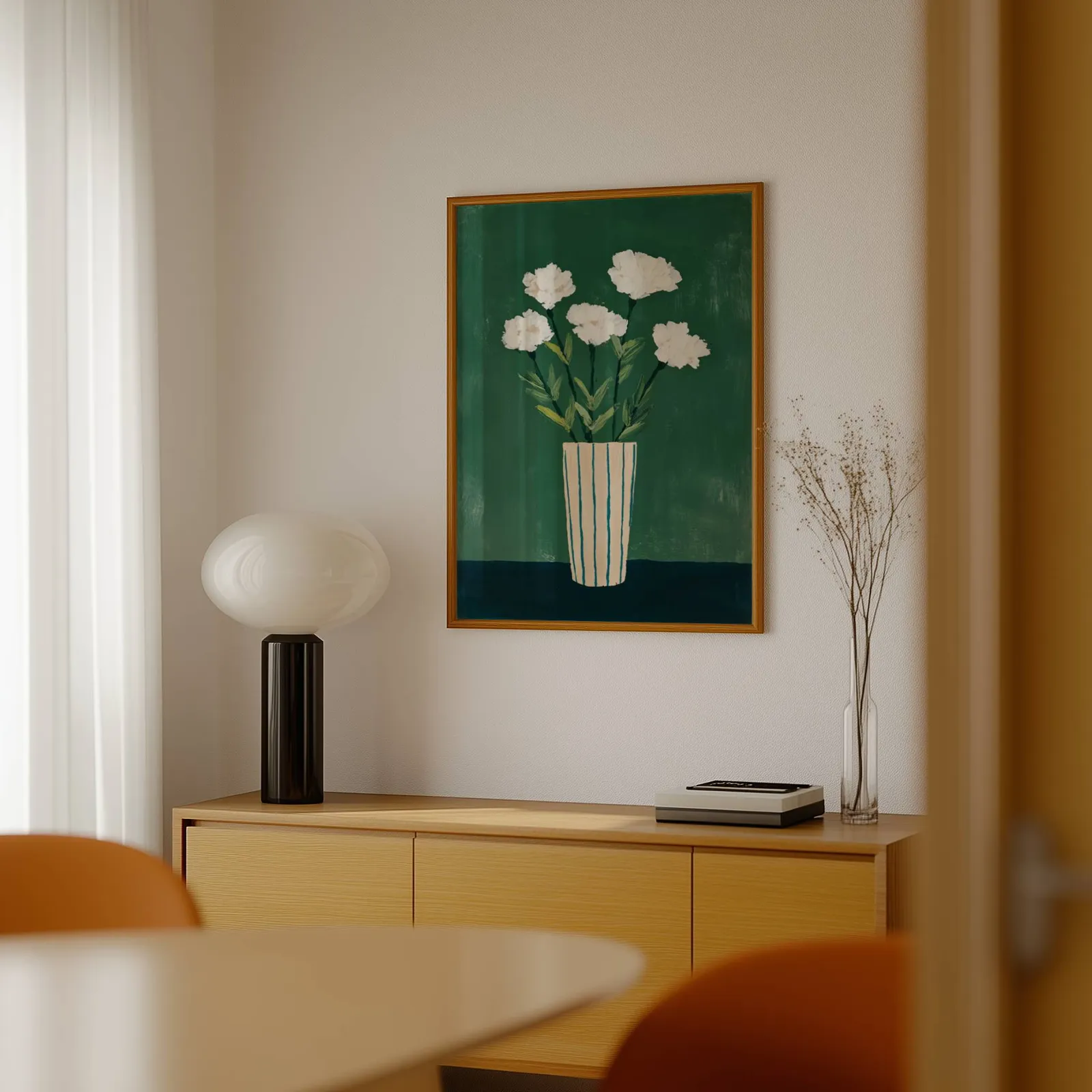 green floral wall art with white flowers in striped vase, above a light wood sideboard beside a bulbous black lamp