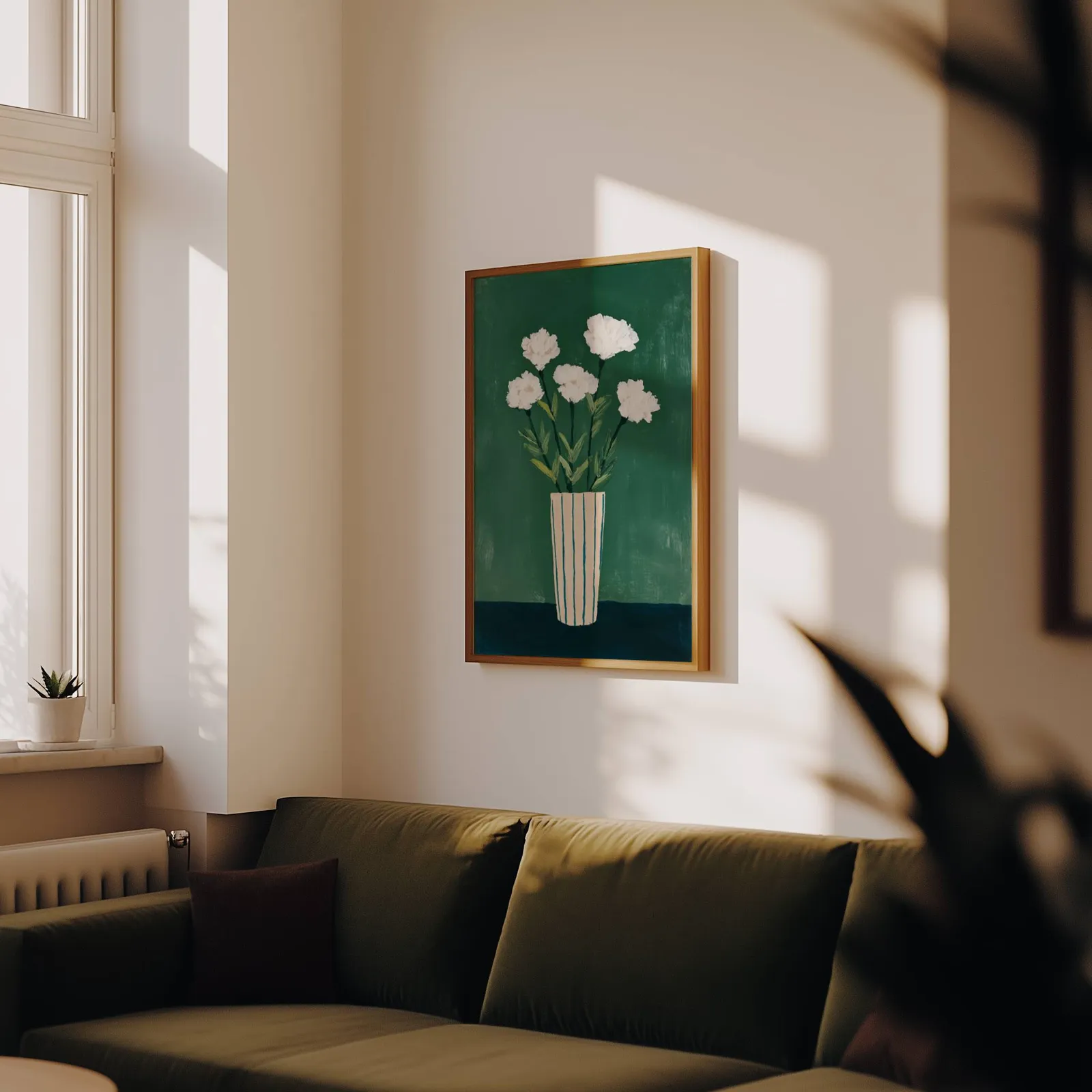 green floral wall art with white flowers in striped vase, above an olive velvet sofa in raking afternoon light