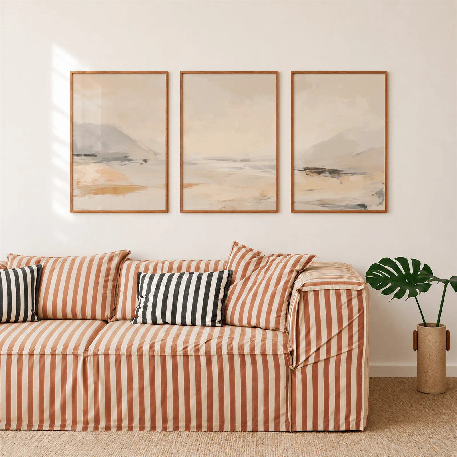 beige abstract landscape wall art set of three, above a rust-striped sofa beside a potted monstera