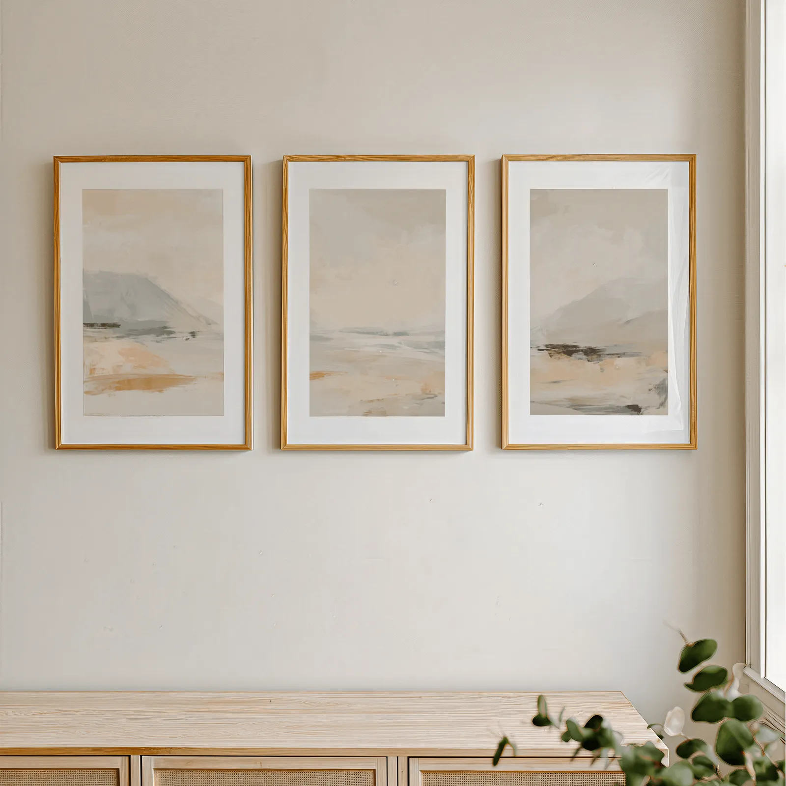 beige abstract landscape wall art set of three, in a row above a light wooden sideboard near a window