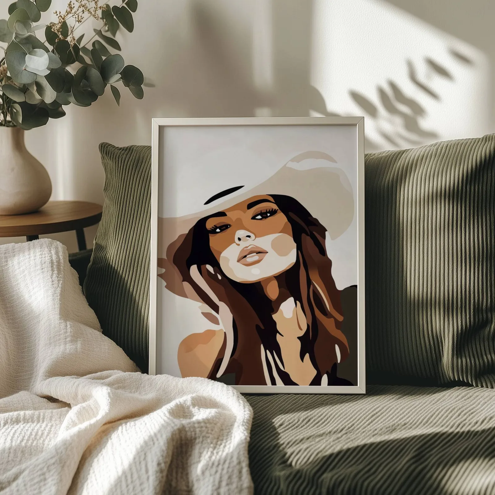 brown abstract woman portrait wall art, propped on an olive corduroy sofa beside a eucalyptus vase