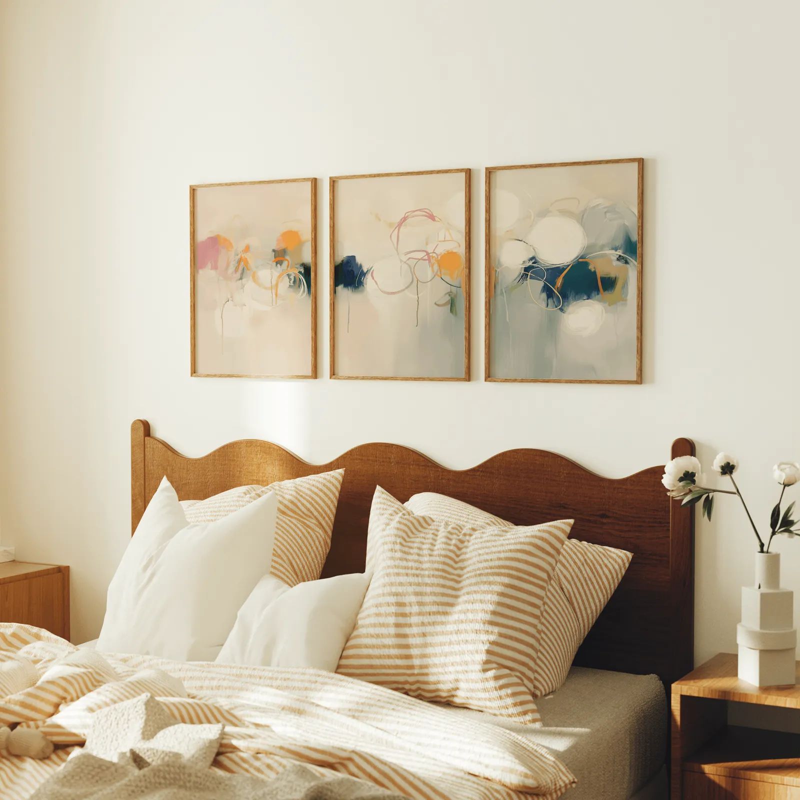colorful abstract triptych wall art in pink orange and blue, above a scalloped wooden headboard with striped pillows