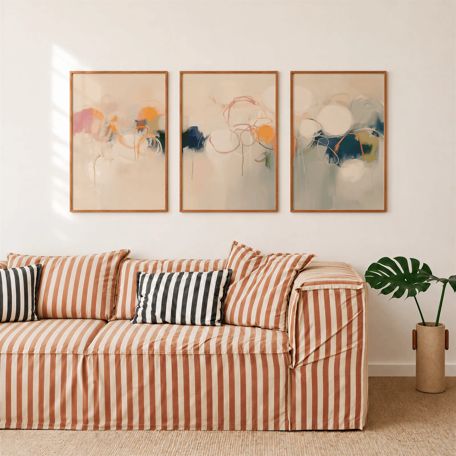 colorful abstract triptych wall art in pink orange and blue, above a rust-striped sofa beside a potted monstera