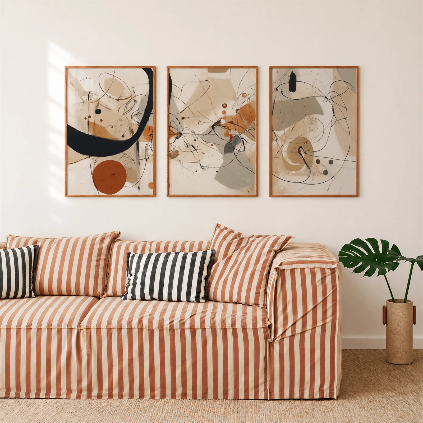 abstract terracotta and black three piece wall art, above a rust-striped sofa beside a potted monstera